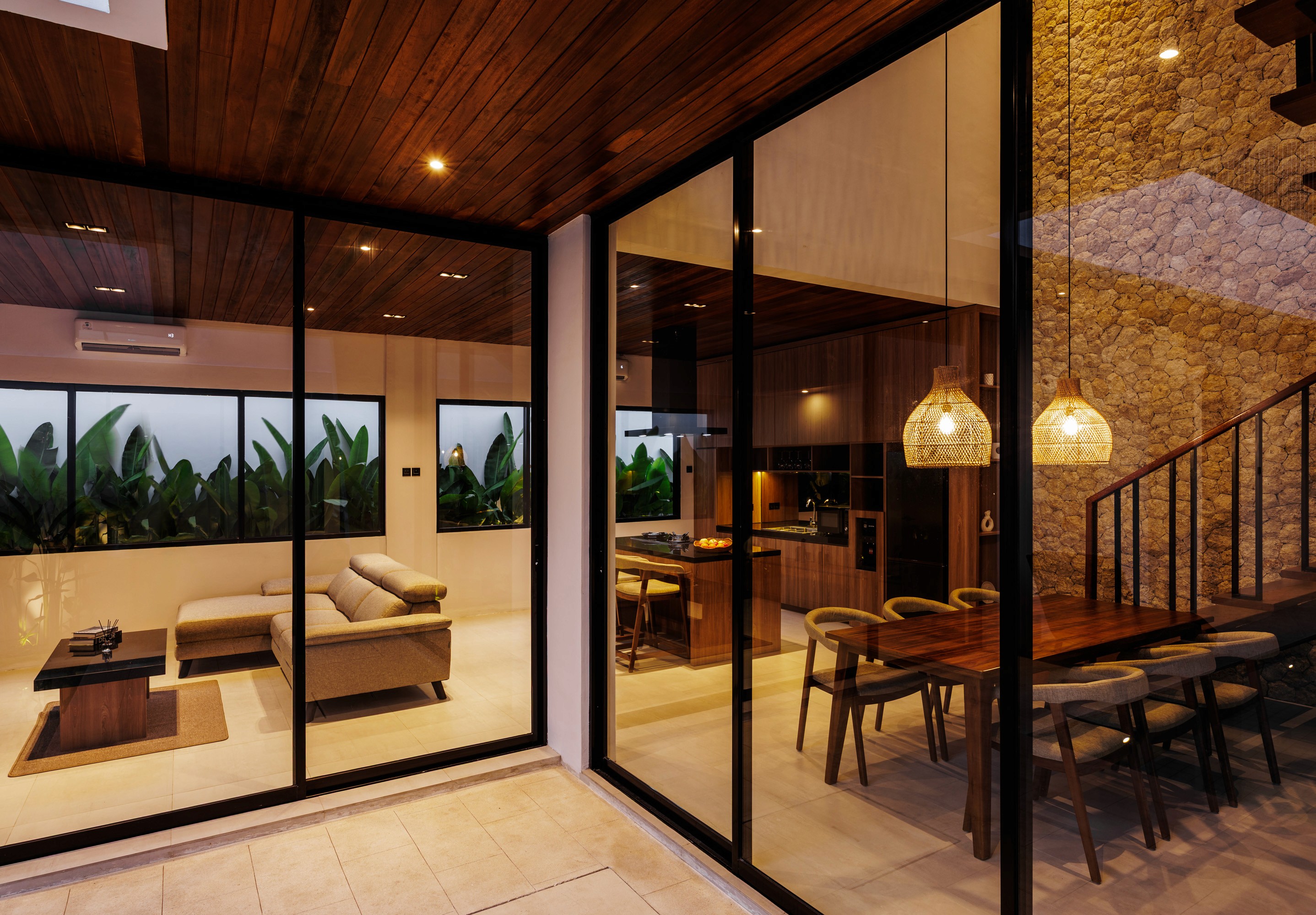 Evening dining area with floor-to-ceiling glass, warm lighting, and textured stone wall.