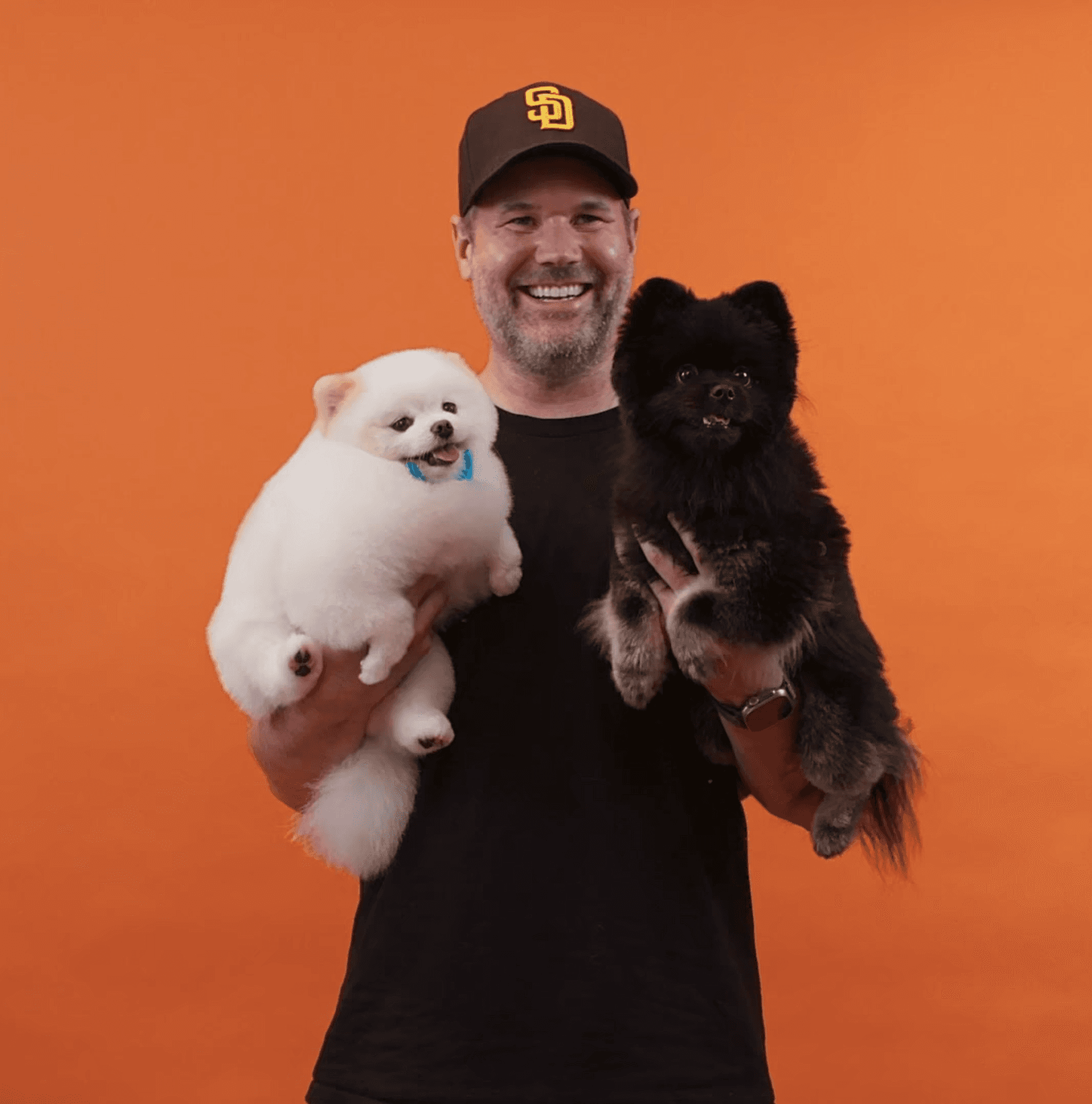 Joyful man holding two fluffy dogs and smiling to convey fun energy, love, and trust in grooming services.