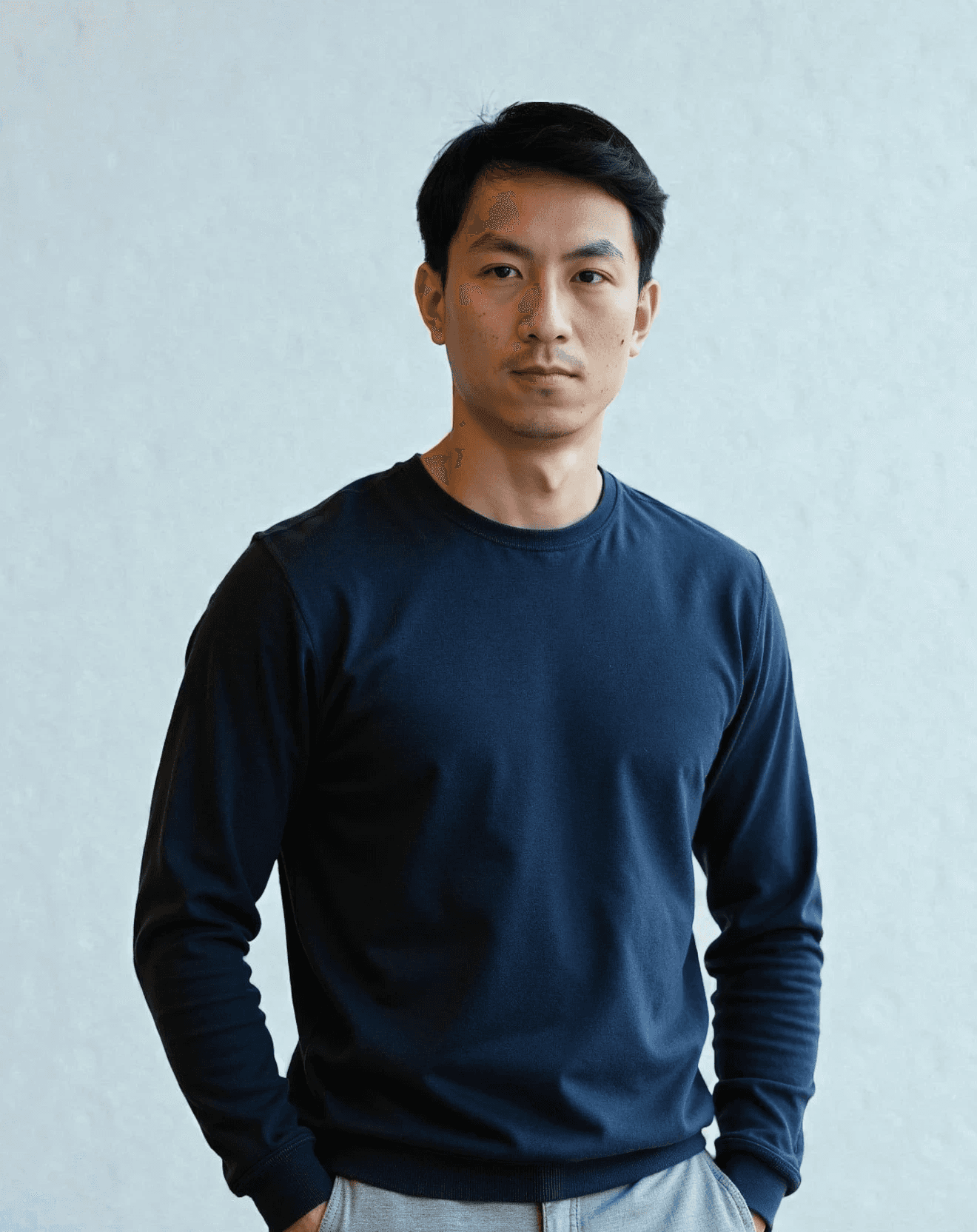 Close-up portrait of a person wearing a gray insulated hooded jacket with the hood up, showing their face framed by the hood against a light background.