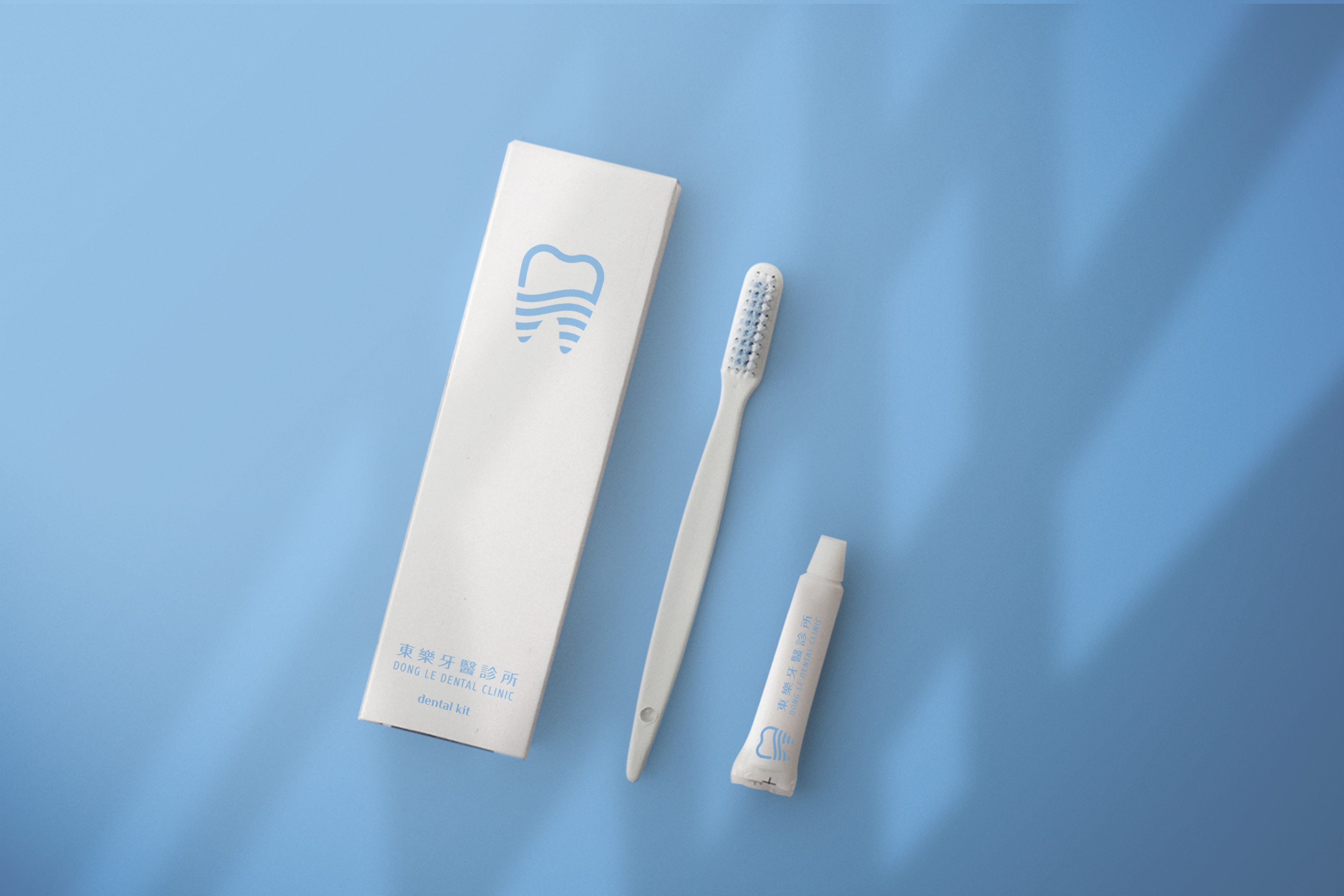 這張圖像展示了東樂牙醫診所的牙齒清潔套裝,包括一把牙刷、一支牙膏和一個包裝盒,包裝盒上有藍色的牙齒標誌和「東樂牙醫診所」及「DONG LE DENTAL CLINIC」字樣。