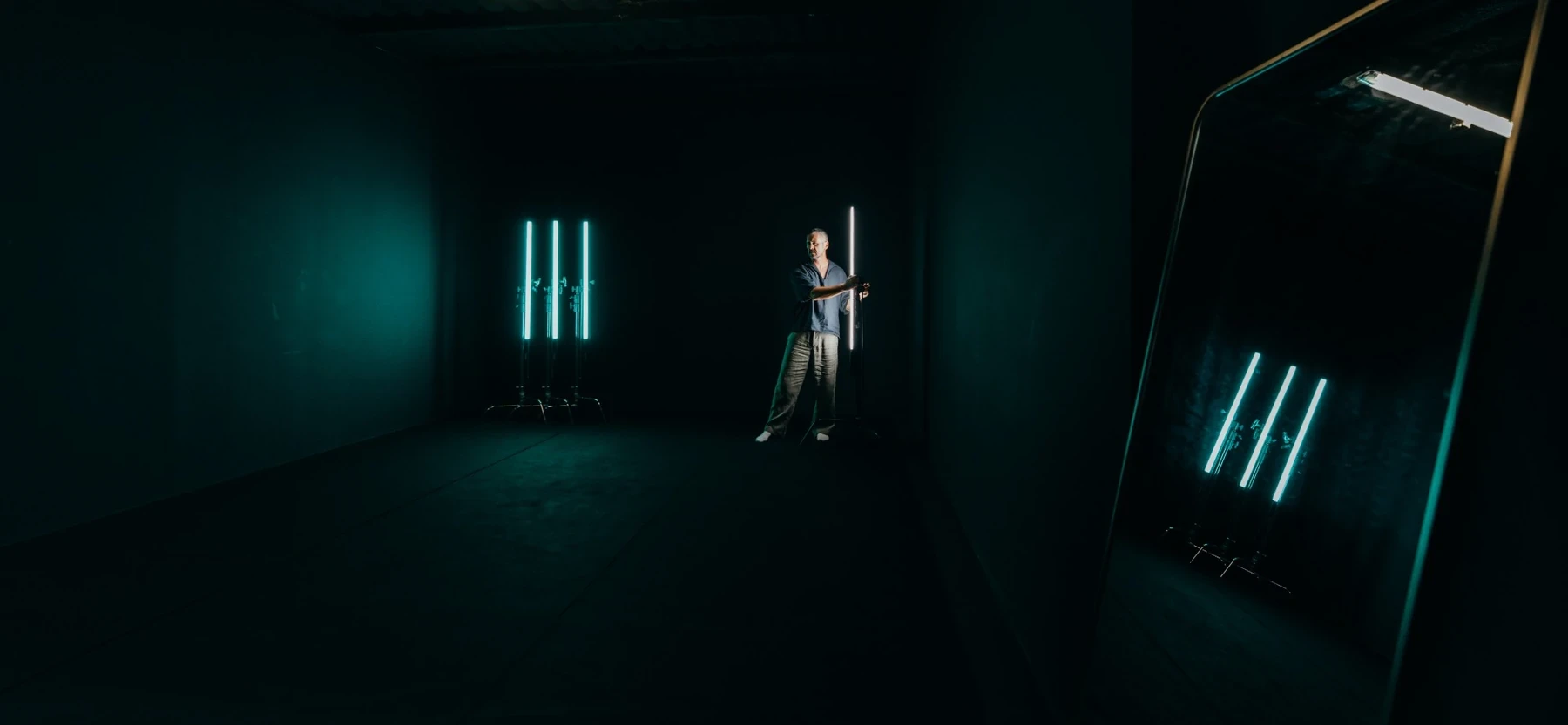 Black cyclorama in Studio 50 lit by teal LED tubes and reflected in a mirror