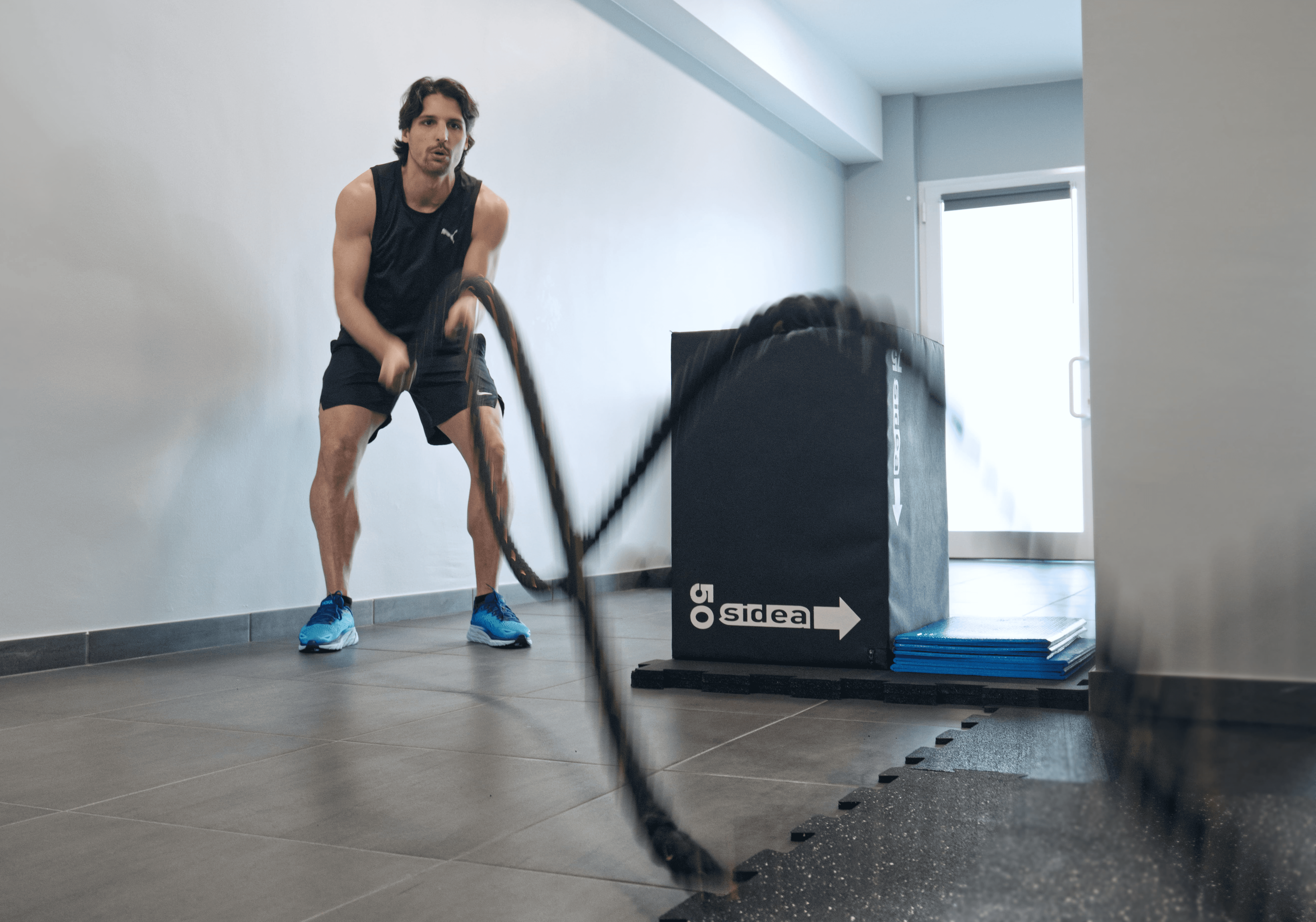 A person in a white outfit sits on a round stool in a spacious, minimalist room. The wall is covered with framed photos surrounding a large screen, creating a serene, contemplative atmosphere