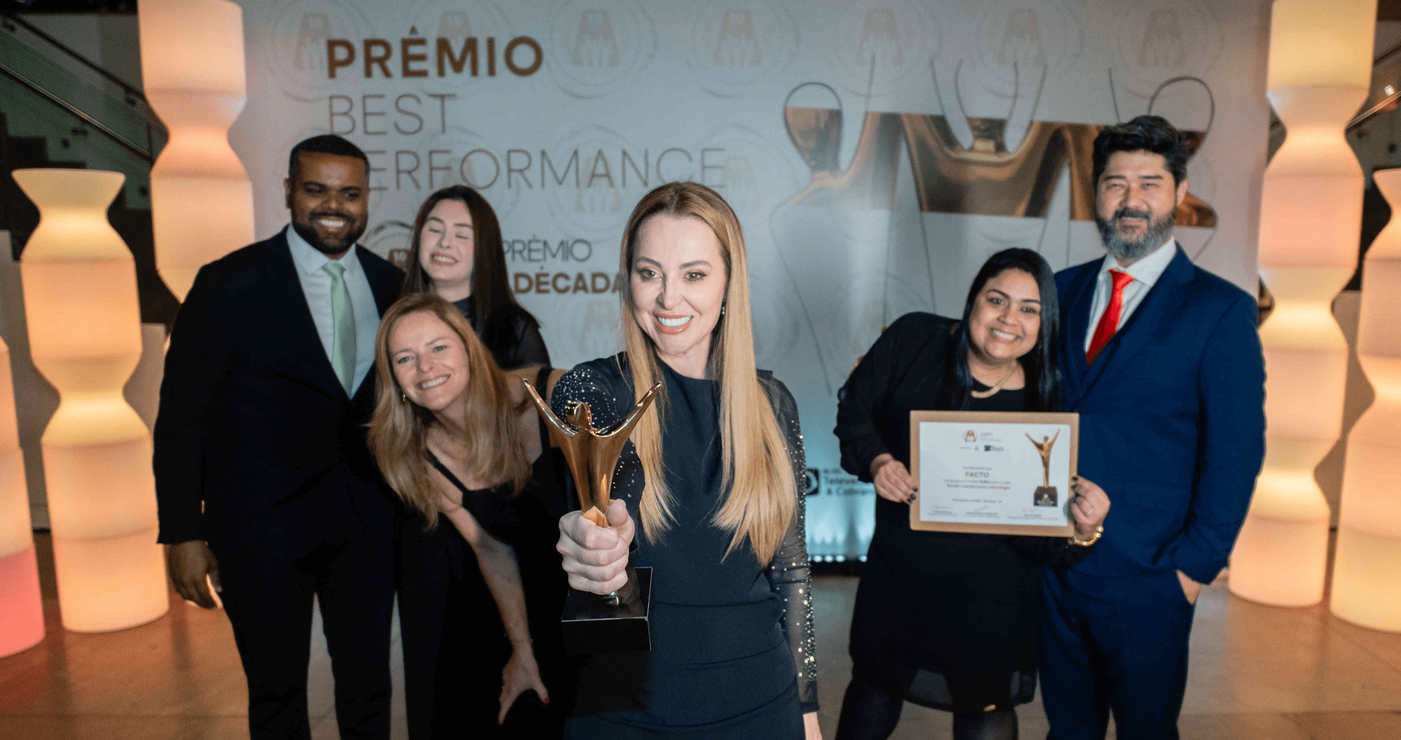 Executivos da Facto posando com troféu prata e certificado no palco do Prêmio Best Performance 2025