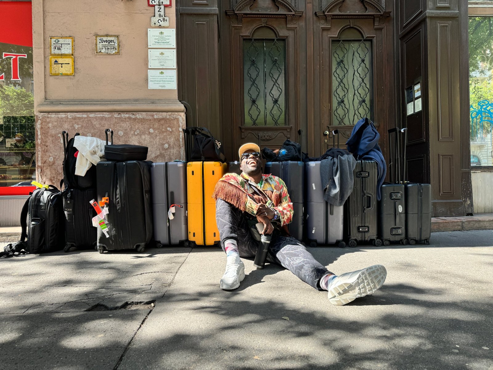 Jubril sitting on a sidewalk in front of a wall of suitcases
