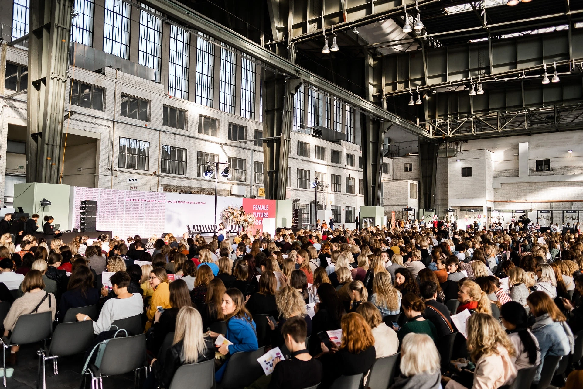 Large audience seated in the daylight-flooded Tempelhof hangar watching the main stage at Female Future Force Day.