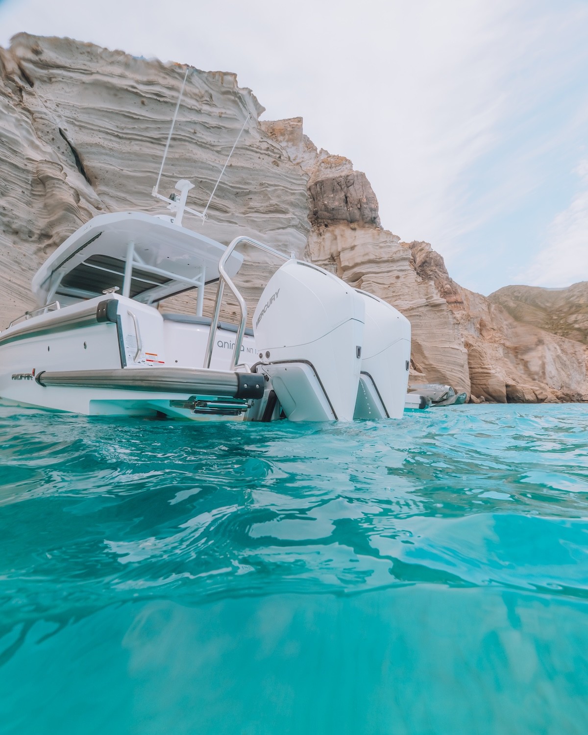 White Axopar 37 yacht named Anima anchored in turquoise waters surrounded by dramatic rocky cliffs in the Cyclades.