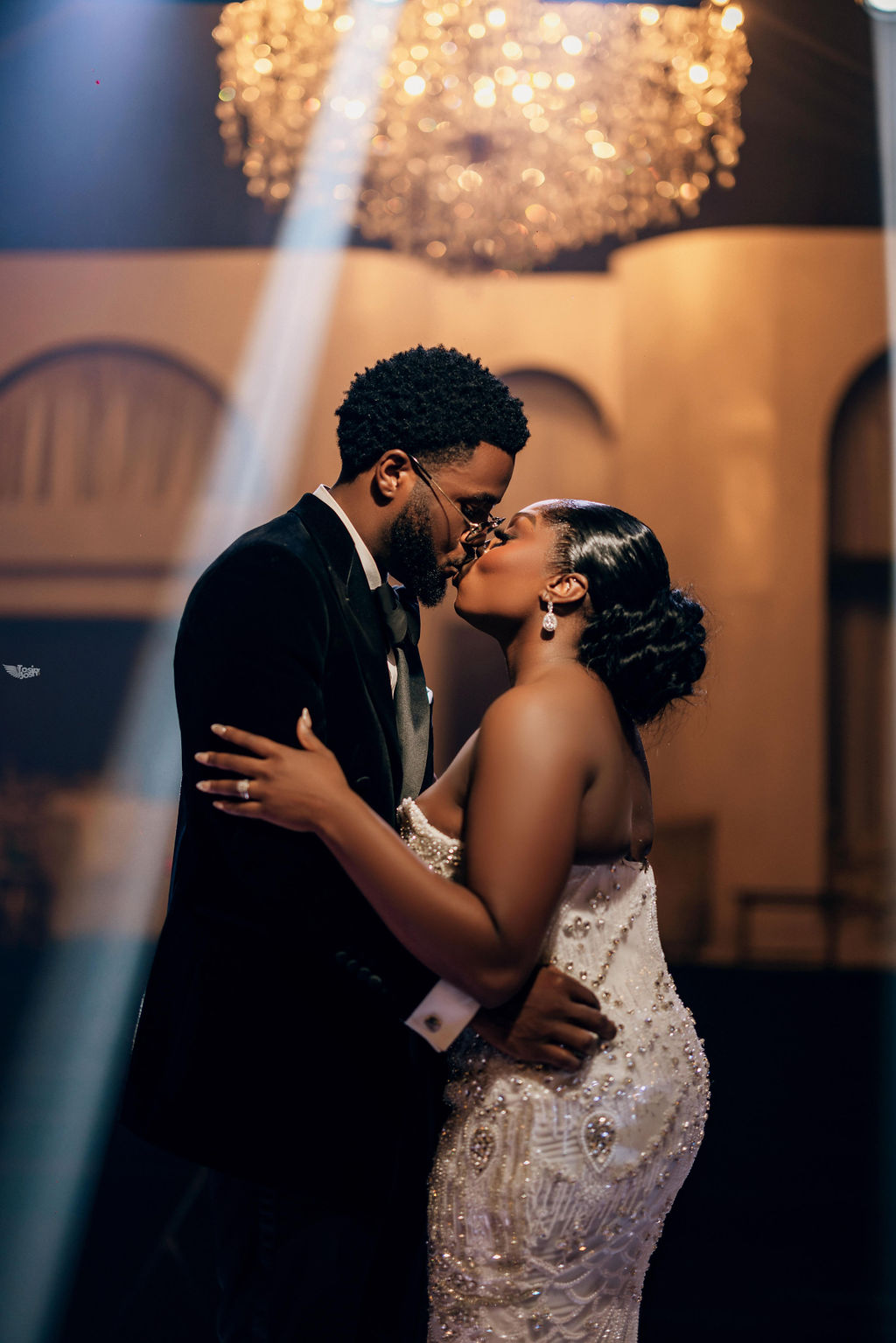 A smiling young man with crossed arms, wearing a plaid shirt and white t-shirt, poses against a dark background.