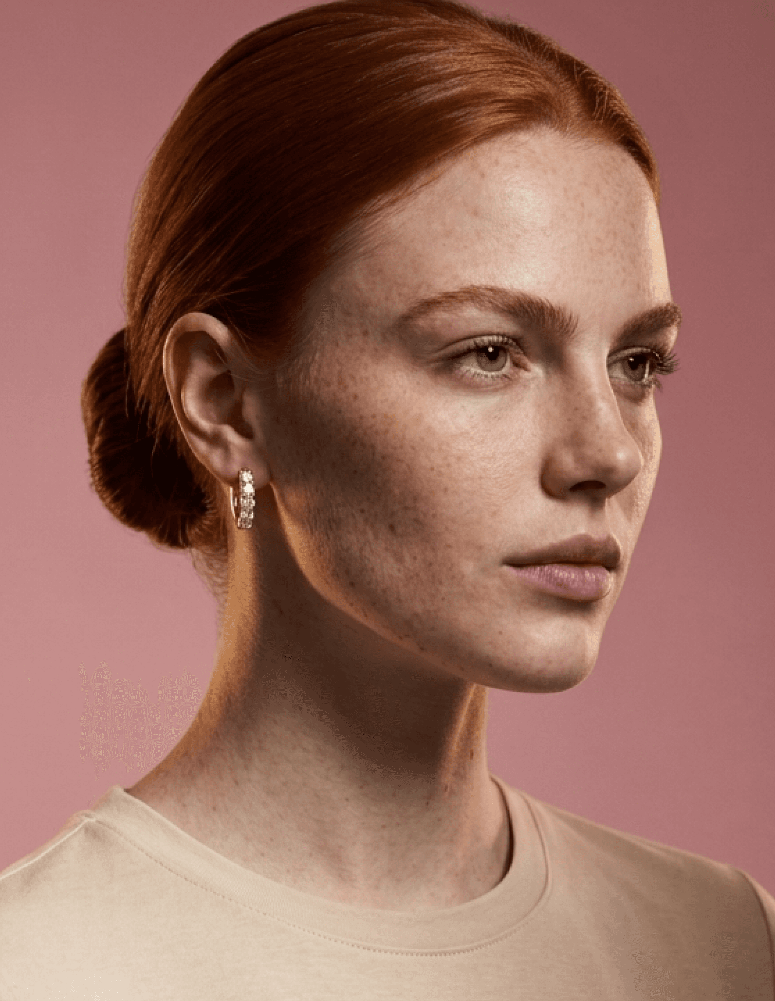 Red-haired woman wearing gold earrings in a soft studio portrait