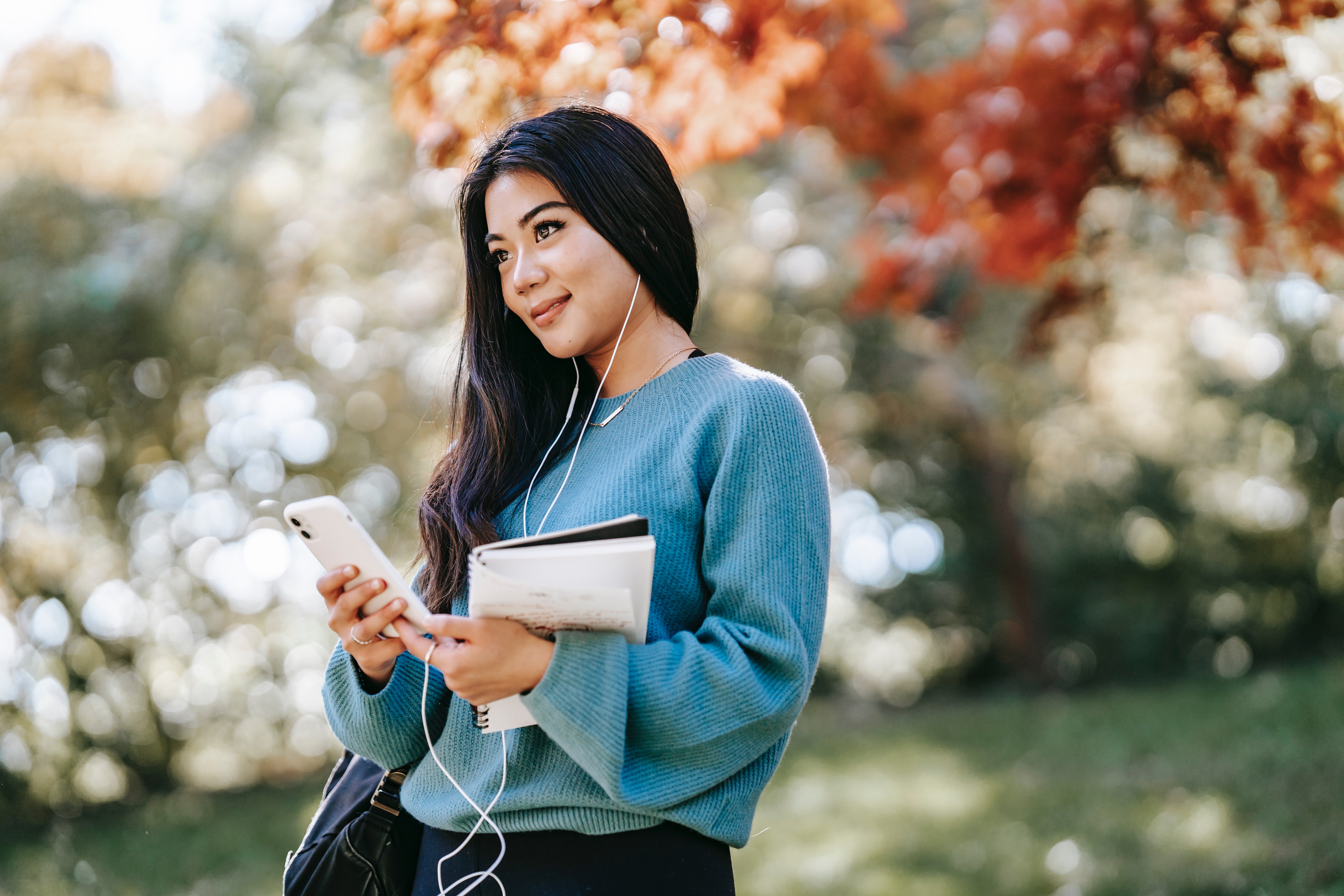 A college-aged woman holds her phone and notebook, looking optimistic
