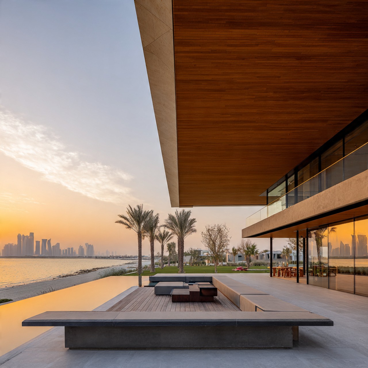 Modern beachfront house with wooden overhang, palm trees, and a sunset over the water. Reflective windows and sleek patio create a tranquil, luxurious vibe.