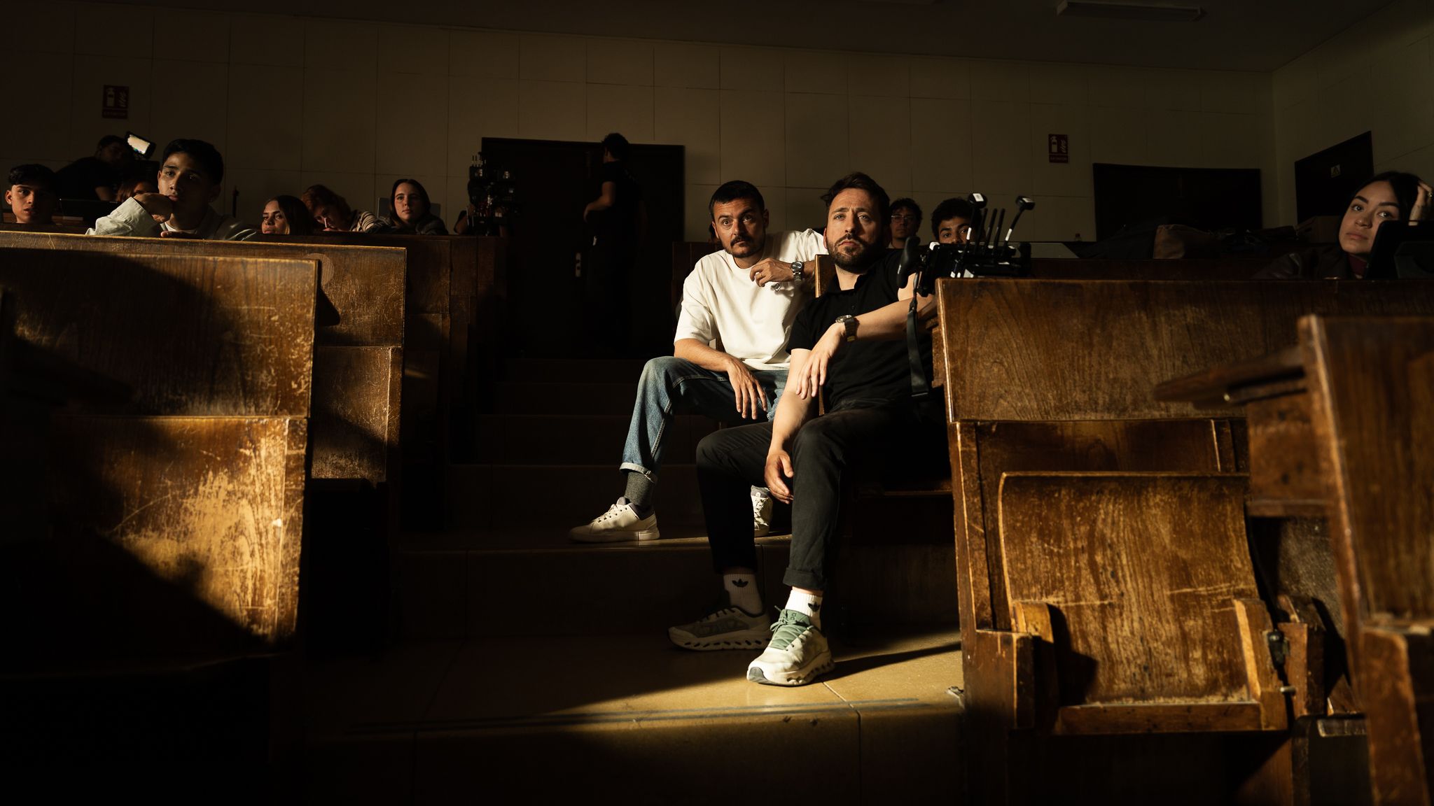 Javier Ramírez sitting with an actor among the benches of the lecture-hall set of Sportybet Promises
