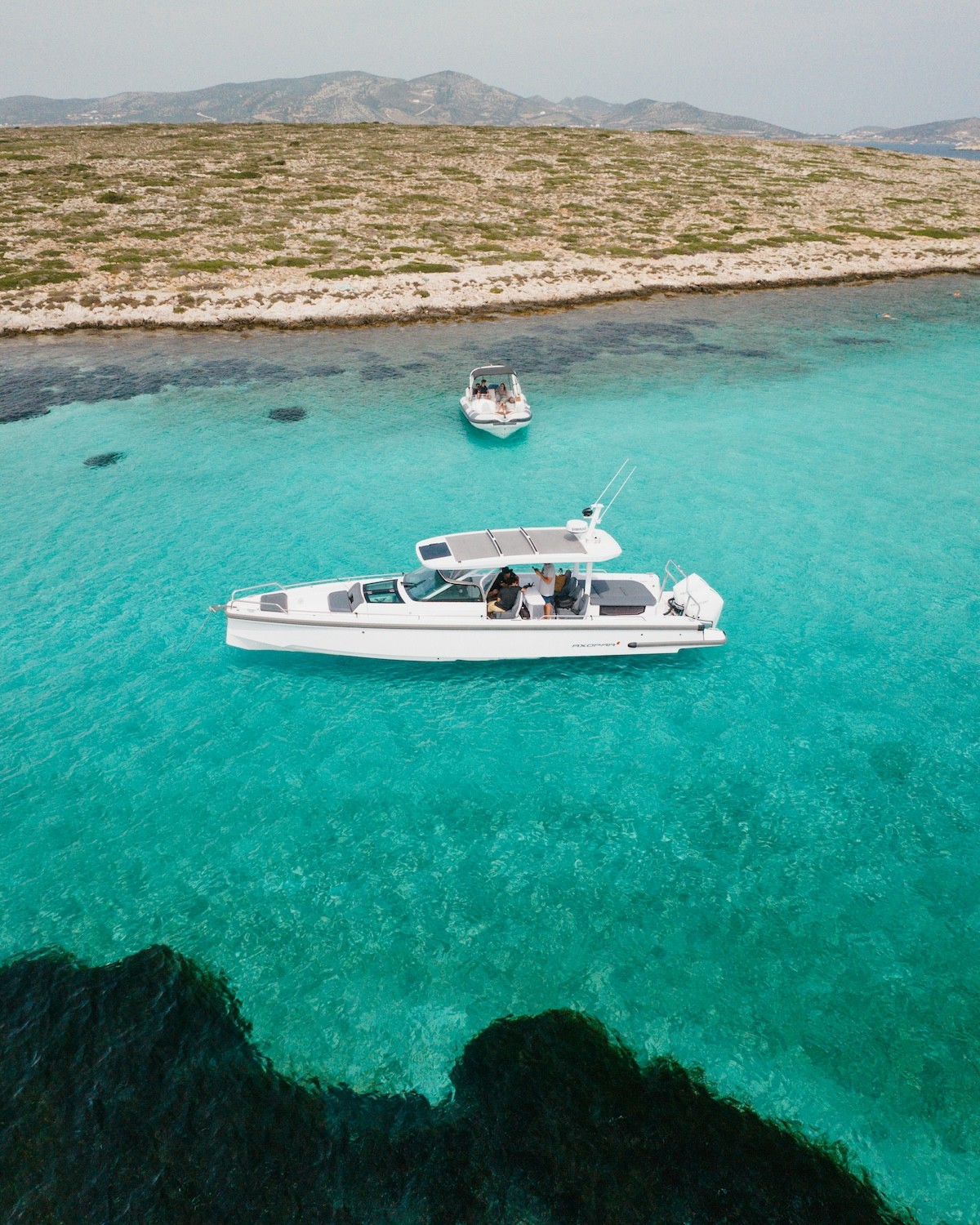 White Axopar 37 motor yacht anchored in turquoise waters near dramatic limestone cliffs with a large sea cave opening.