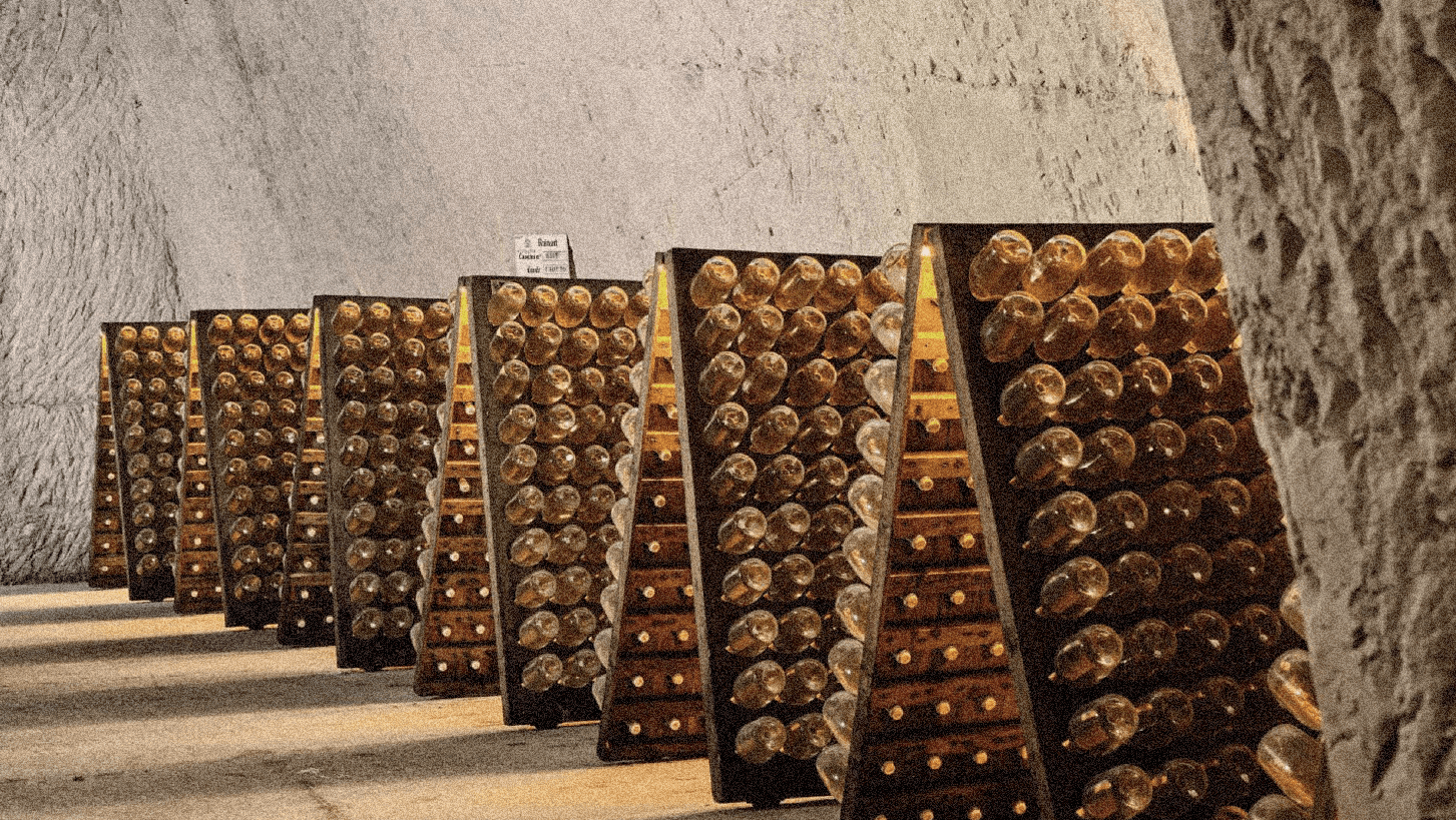 An underground wine cellar lined with champagne bottles resting on riddling racks — a quiet tribute to craftsmanship and the heritage of French winemaking.