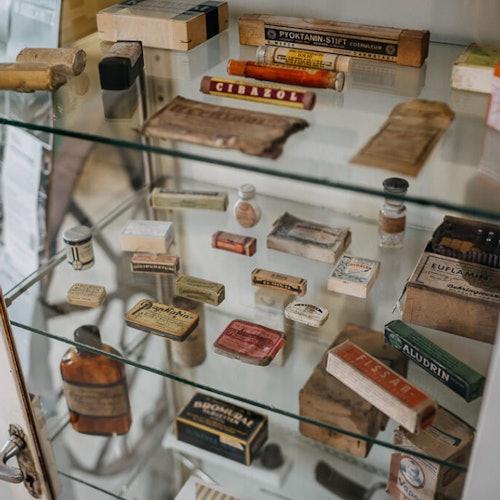 A glass display case filled with various vintage medical and pharmaceutical items, including bottles, boxes, and tubes.