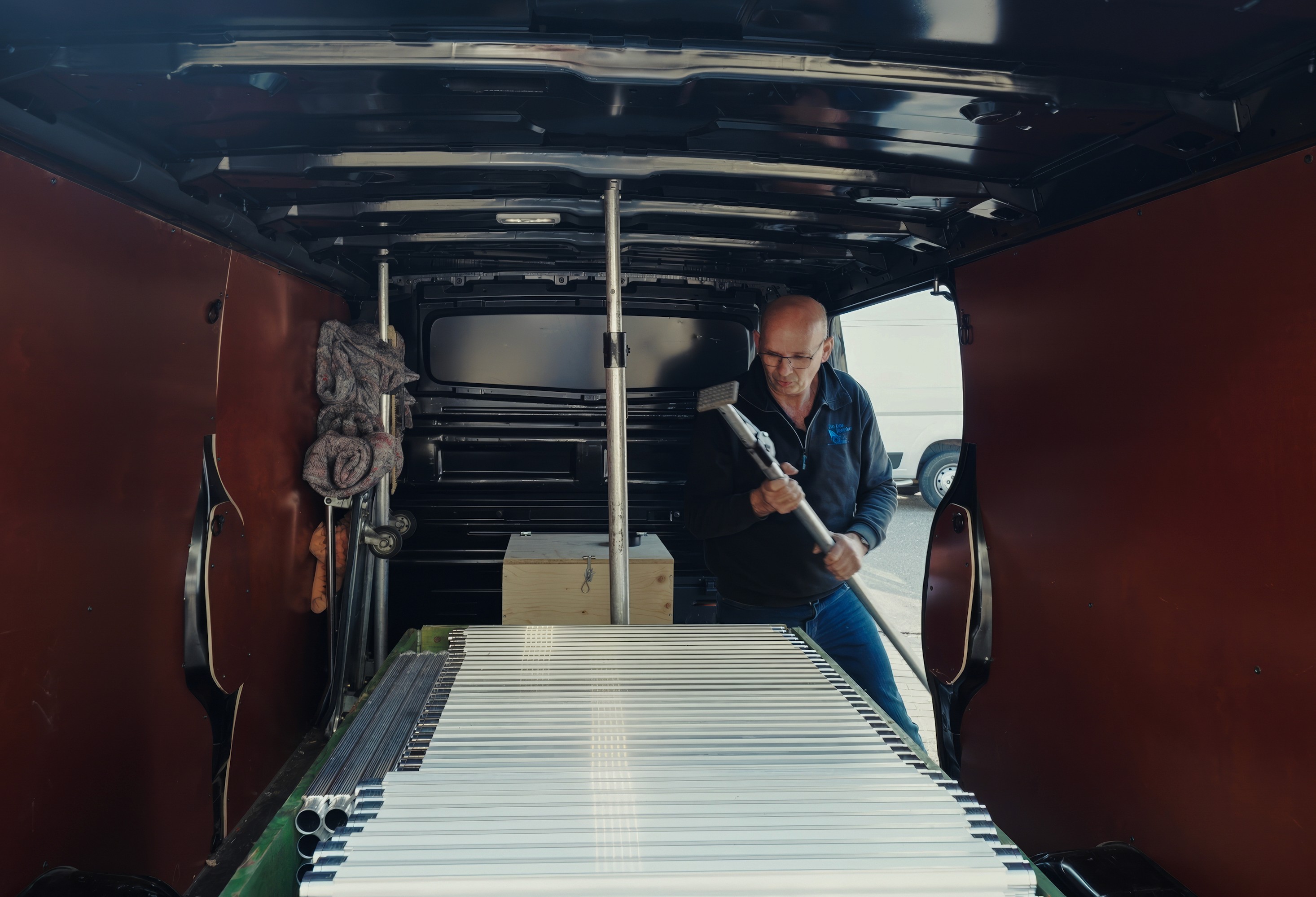 Man in de laadruimte van een zwarte Van Ede Koeriers bestelbus bezig met het vastzetten van pakketten voor transport.