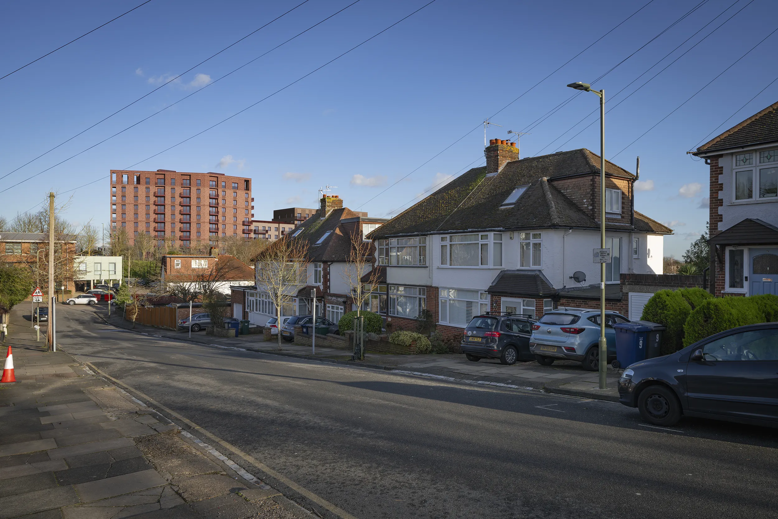 Type 4 AVR Level 1 wireline verified view due east along Woodfall Avenue, High Barnet, showing the upper levels of Building A and a partial glimpse of Building B beyond semi-detached houses and the Vale Drive care centre.