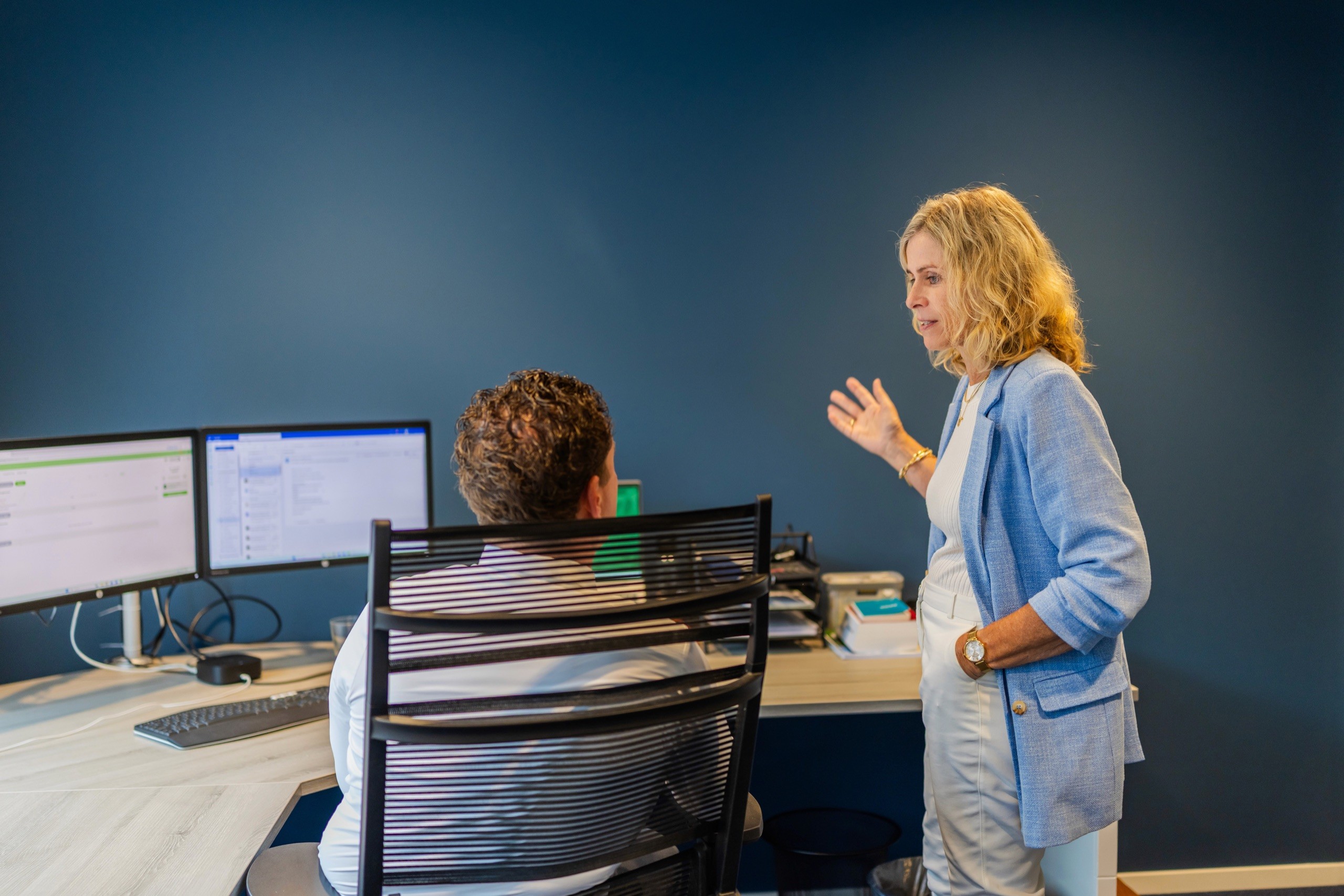 Medewerker geeft uitleg aan een collega achter de computer