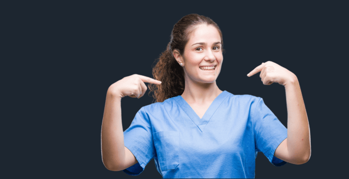Smiling healthcare worker in scrubs pointing at herself on a dark gray background