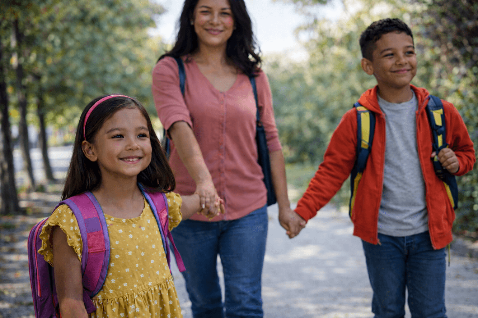 Smiling mother walking with her children carrying school backpacks, reflecting safe, nurturing, and high-quality early learning at LEAO Tampa.