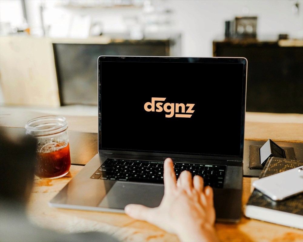  Hand tippt auf Laptop an aufgeräumtem Schreibtisch mit Notizbuch und Getränk im warmen Licht 