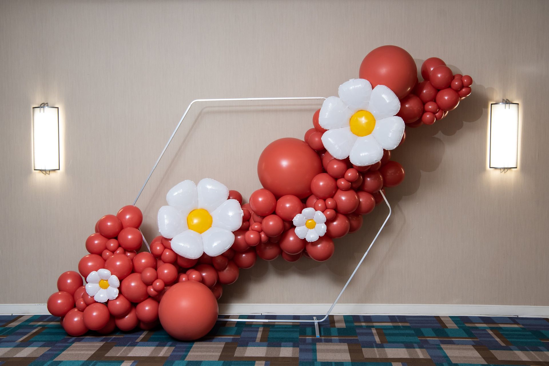 Red and white balloon garland with large flower-shaped balloons decorating a wall by Be Bold Balloons