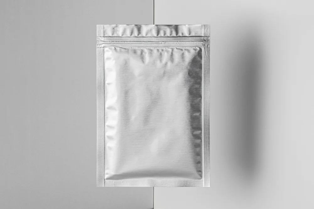 Silver flat pouch packaging mockup with bold black and yellow accents, showcasing a metallic texture. The pouch is centered against a split black-and-white background, creating a clean, modern aesthetic.