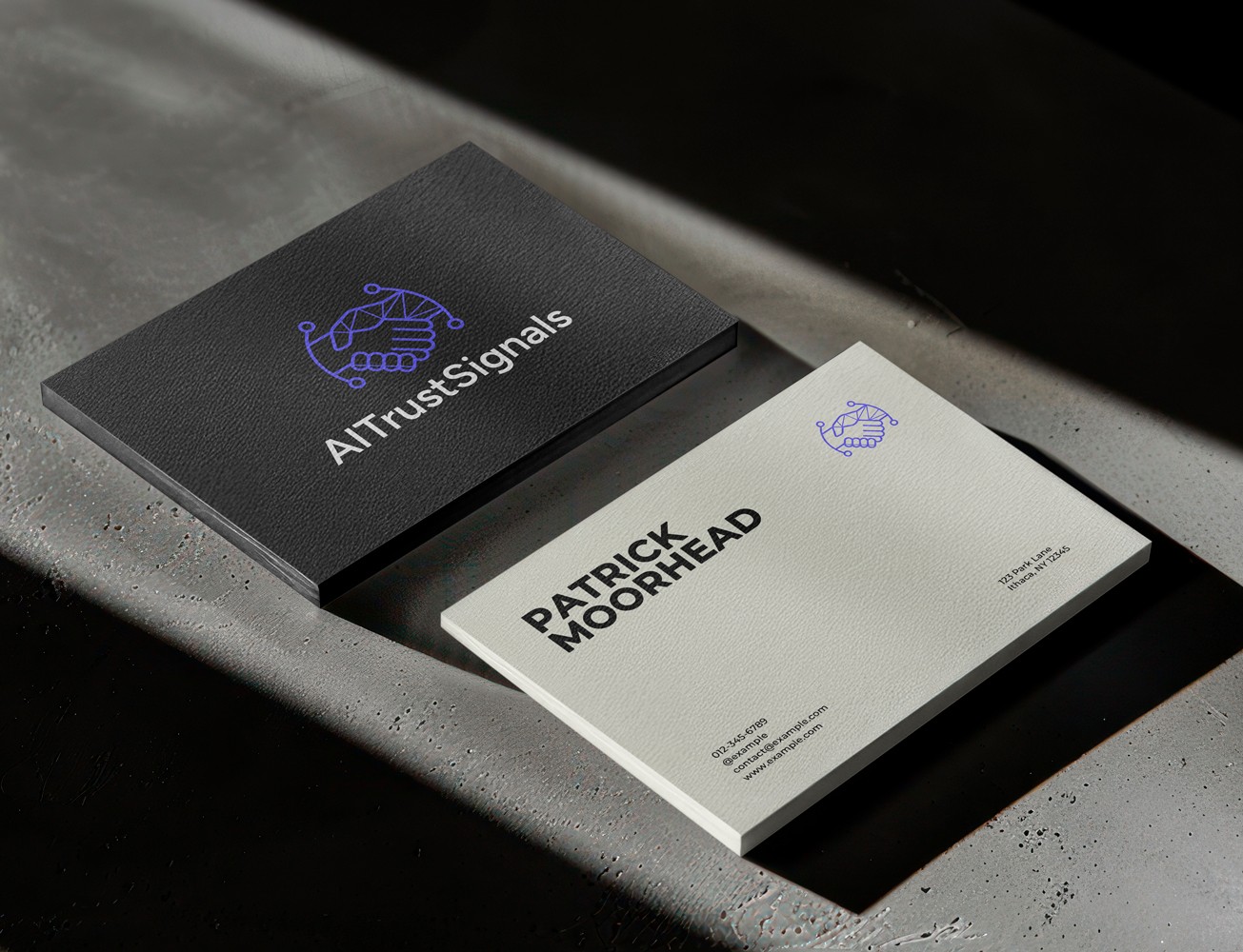 Stacked black and white business cards on a concrete table, featuring the AI Trust Signals digital handshake logo and contact information for Patrick Moorhead.