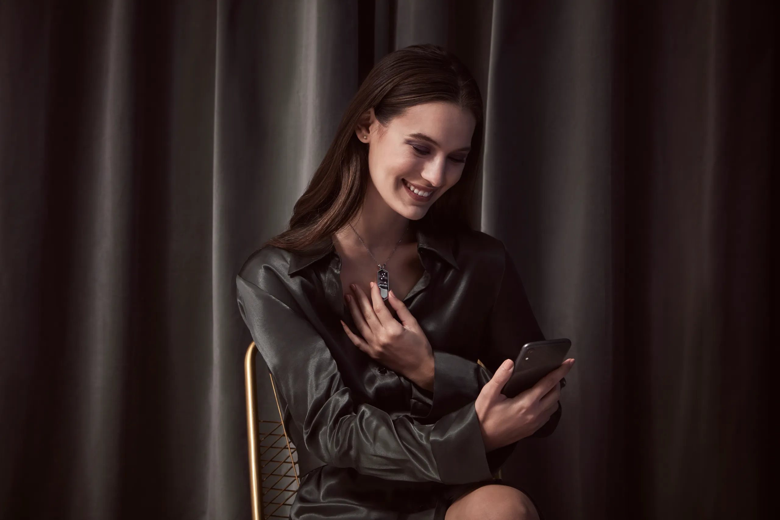 Woman holding a Talsam smart jewelry charm while looking at her phone
