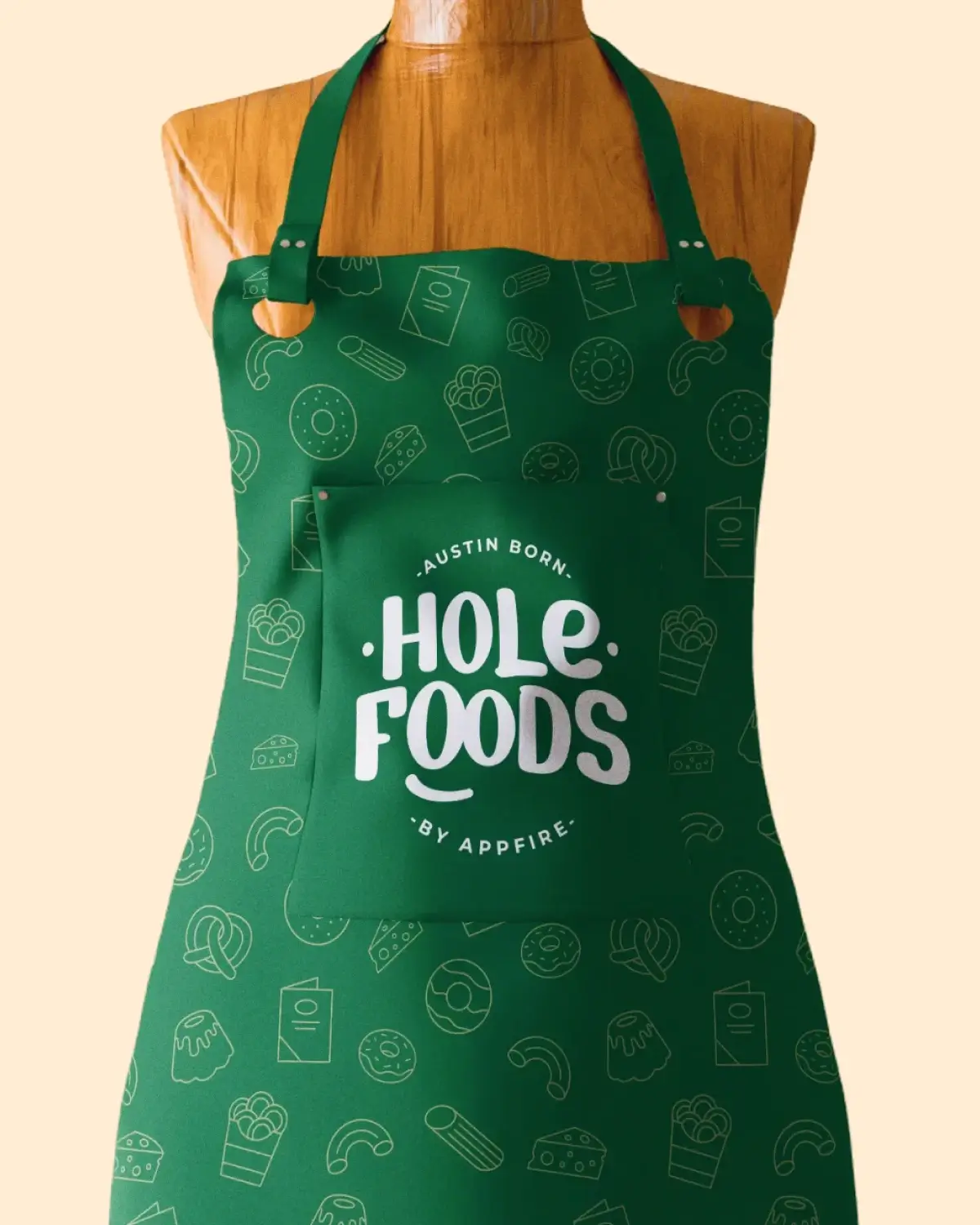 A green apron with "Austin Born, Hole Foods by Appfire" printed in white over a white shirt. The apron pocket has a playful food icon pattern.