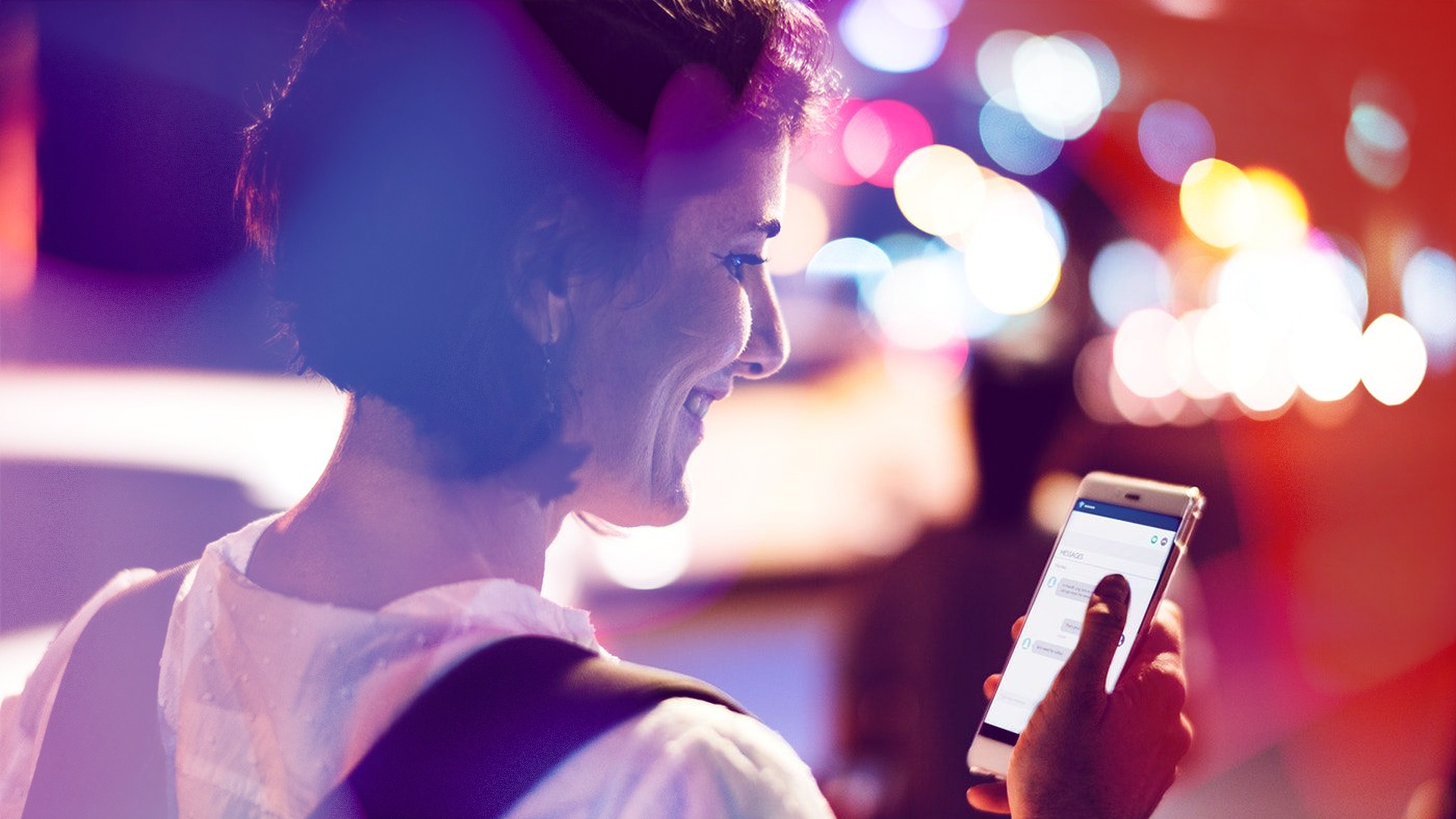 A woman on a street outside looks at her phone, smiling