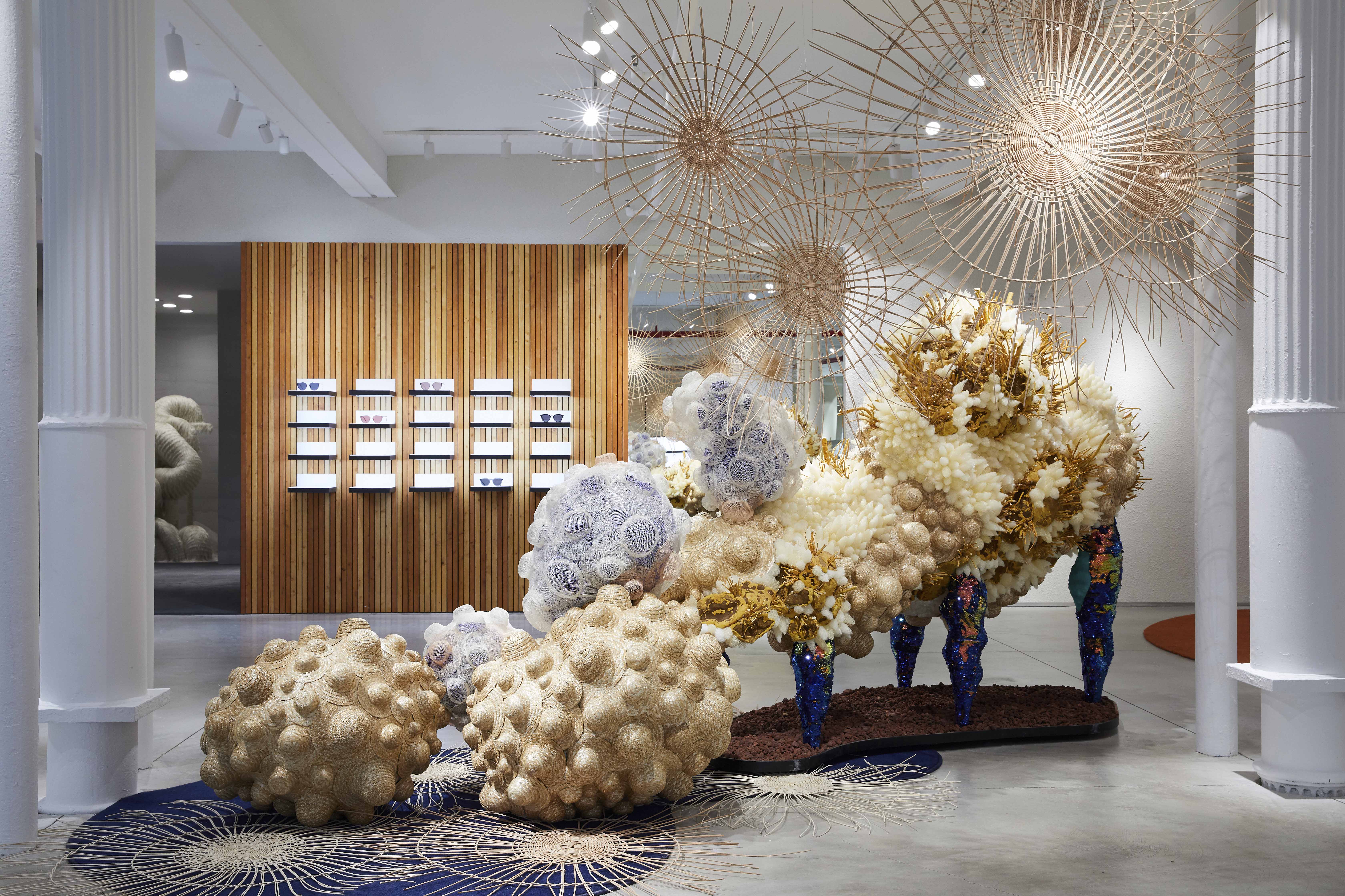 Inside a Gentle Monster store, an elaborate sculptural installation of organic, coral-like forms fills the space beneath decorative hanging structures in a bright, gallery-like interior.