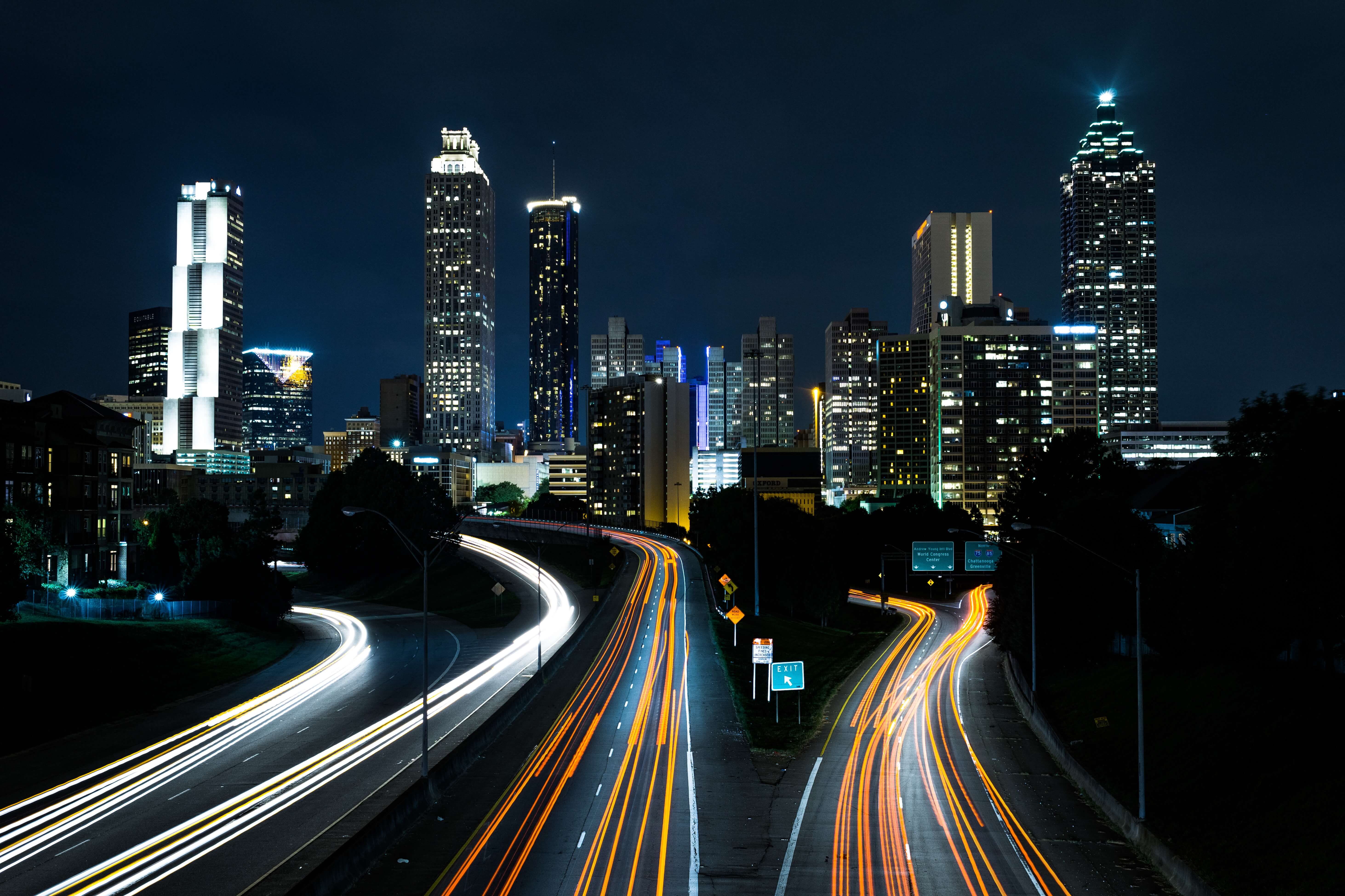 Nighttime cityscape of Atlanta with illuminated skyscrapers; highway in foreground shows light trails from passing cars.