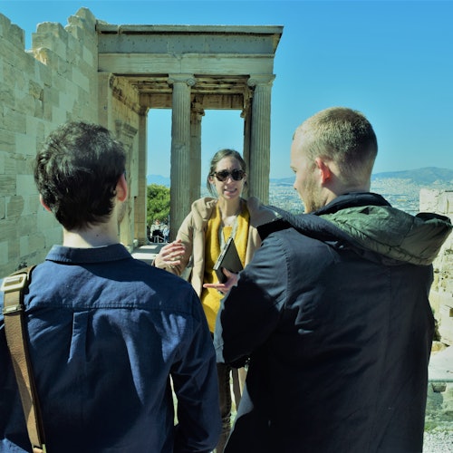 三个人在晴朗的蓝天下，于古老的石柱和遗迹旁交谈。