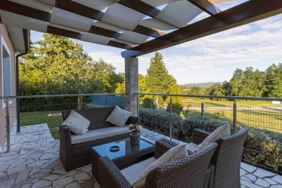 Outdoor patio seating area with wicker furniture, stone flooring, and a pergola overlooking trees and open views.