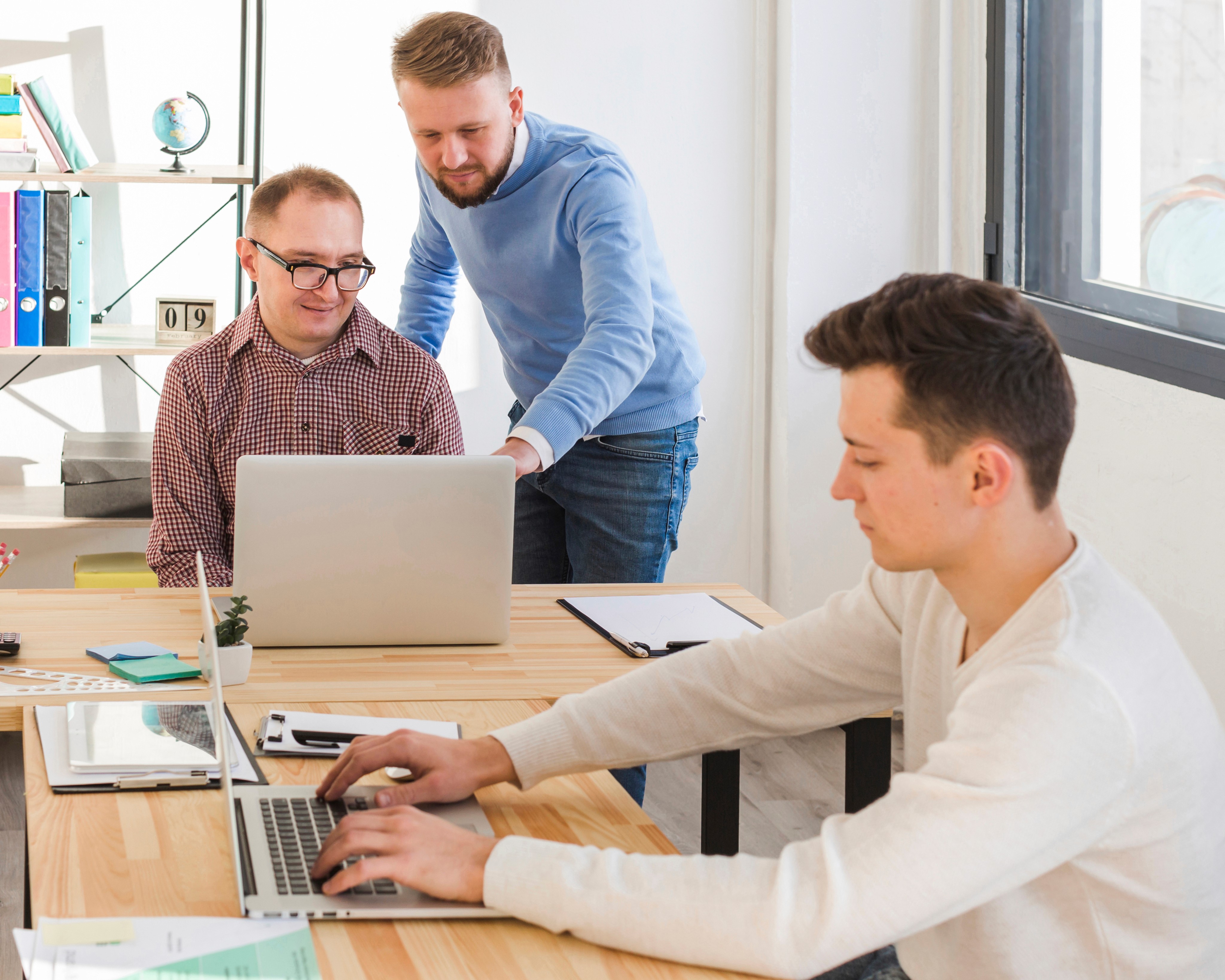 Three men working on laptops together in a bright modern office.