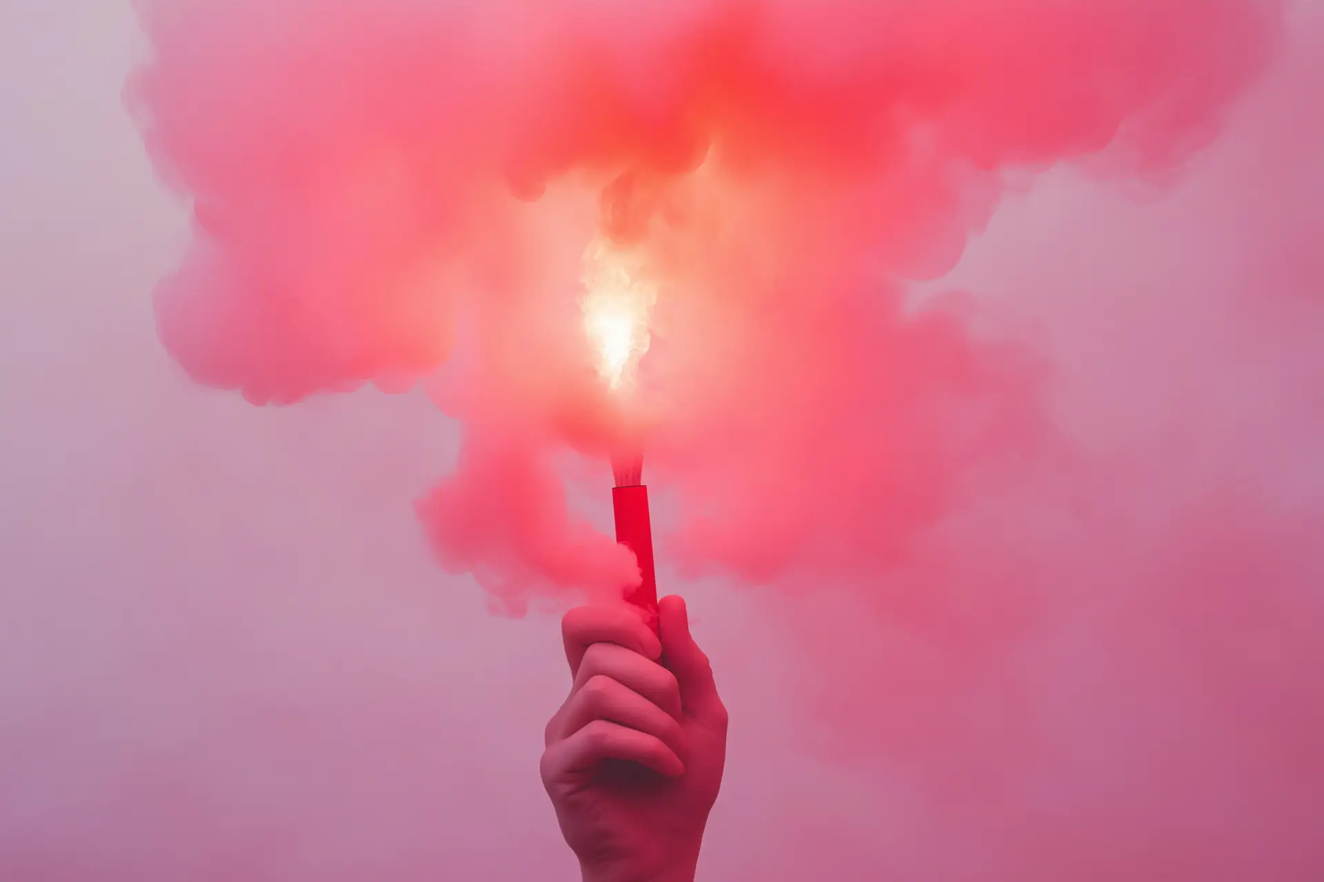 Hand hält eine brennende rote Handfackel, dichter roter Rauch steigt auf