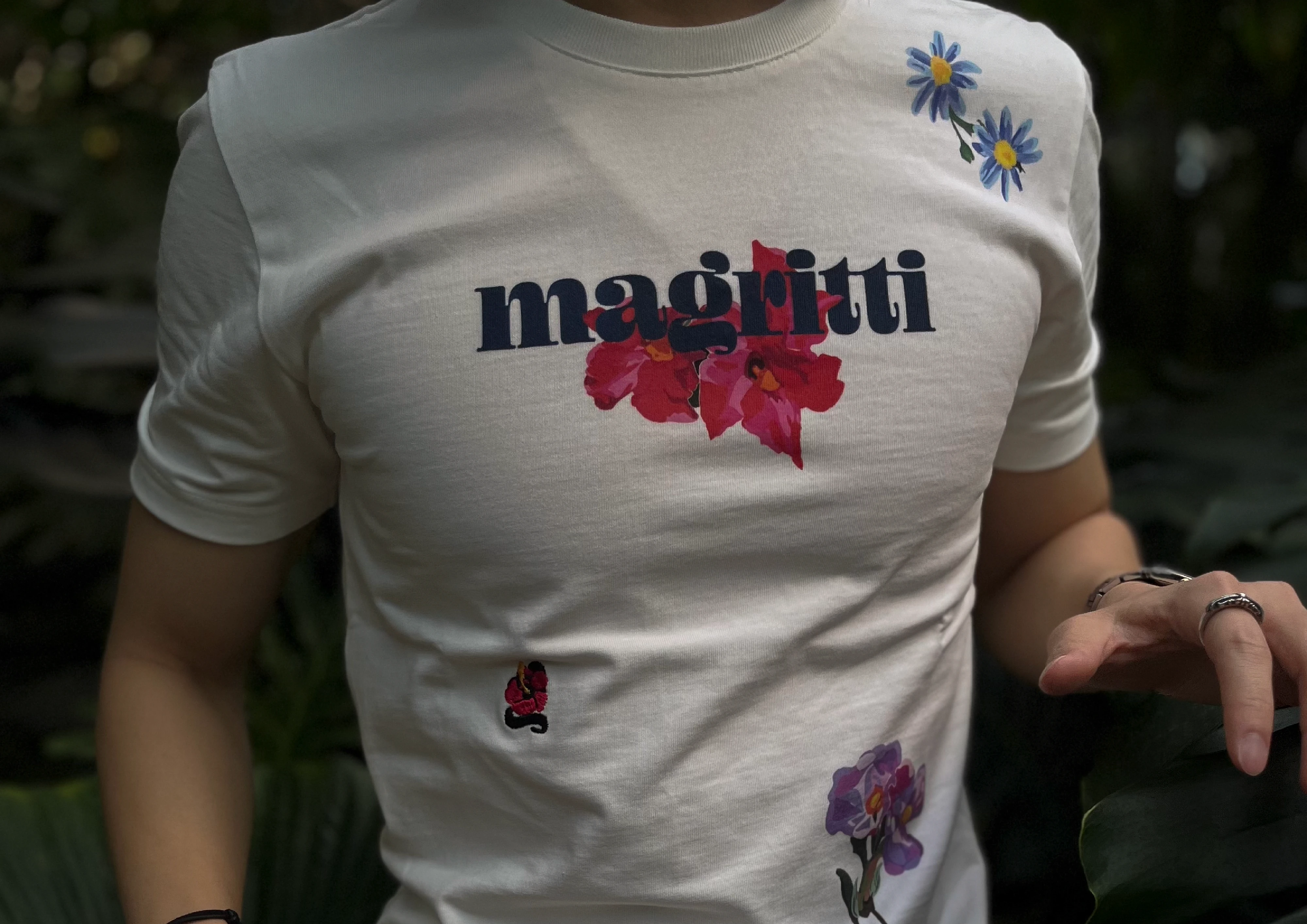 Close view of a white shirt worn on the body, with blue daisies at the shoulder and a small embroidered flower below the chest.