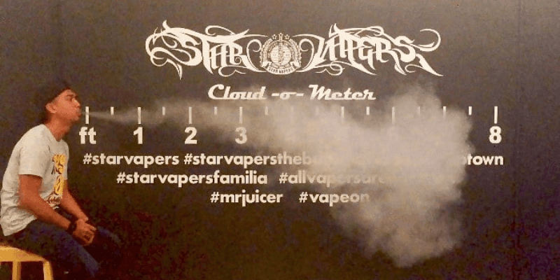 Seorang lelaki menghembus asap vape di depan papan tanda kedai Star Vapers.