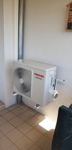 Pompe à chaleur air-eau de la marque Toshiba placée dans le coin d'une façade, à côté d'une goutière