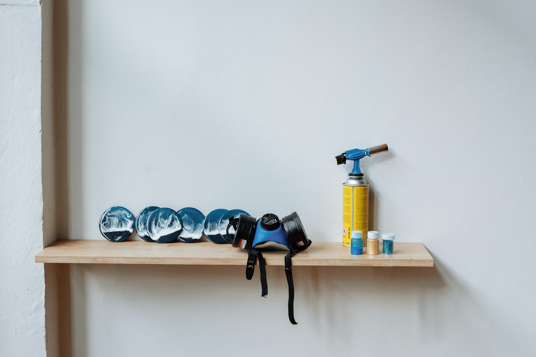 A wooden shelf displaying resin art, blow torch, and safety gear, illustrating a creative workspace.
