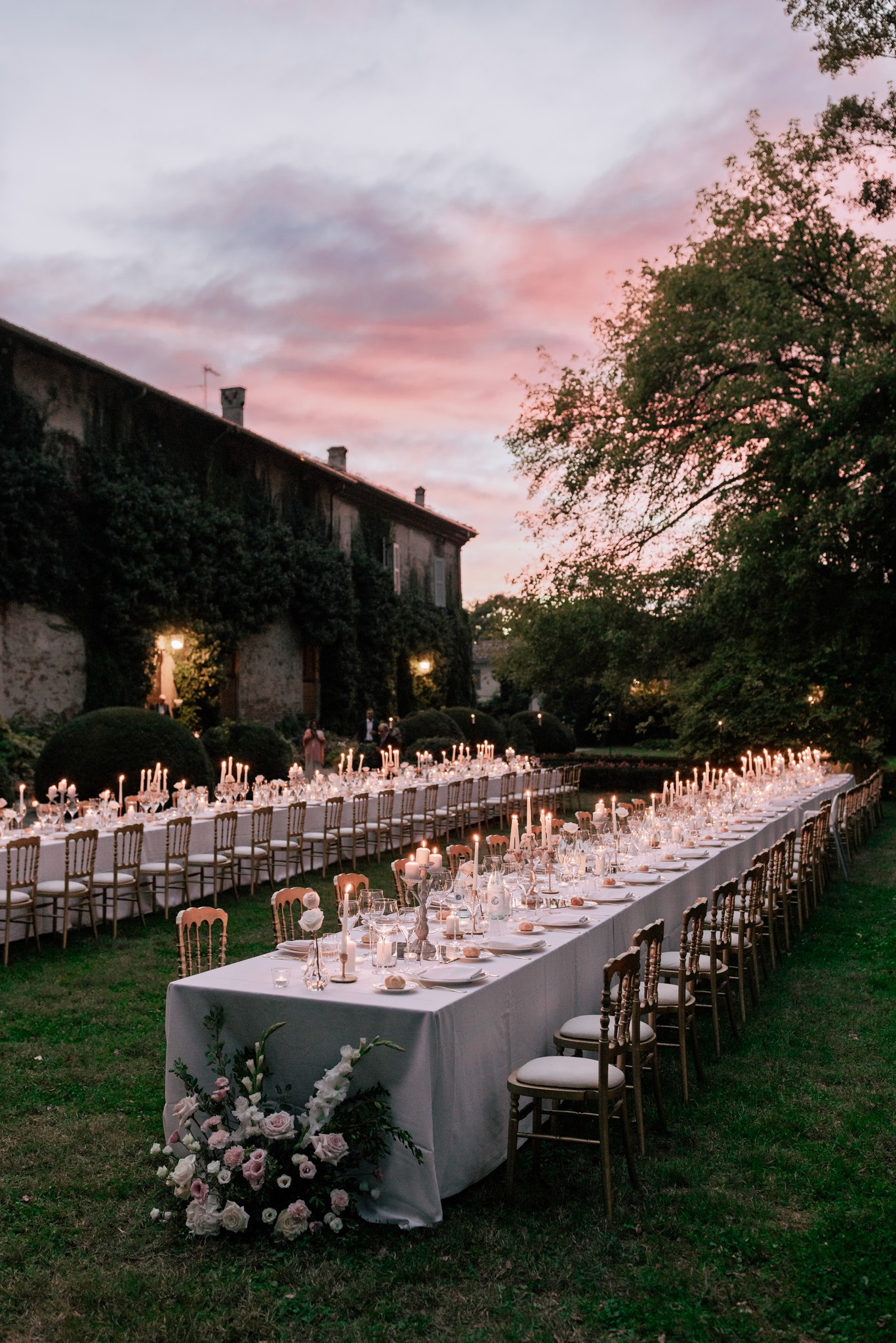 Ricevimento matrimoniale a Villa Ferrari al tramonto, tavoli illuminati da candele nel parco, cielo rosa al crepuscolo