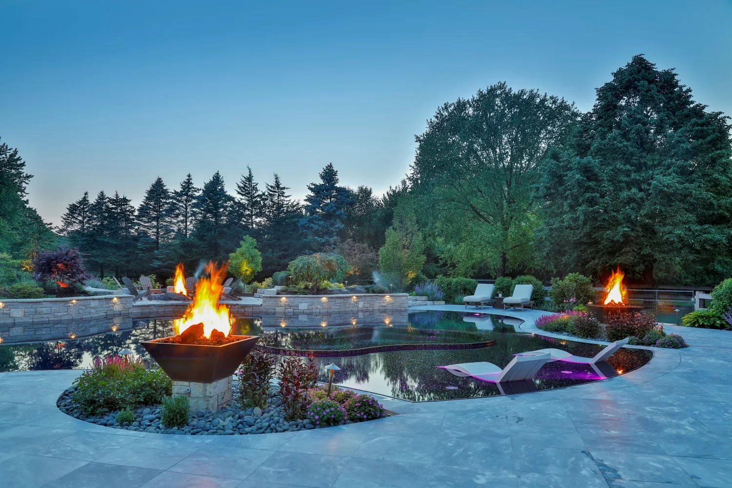 The pool at twilight with fire bowls lit, the mosaic floor mirroring the sky.