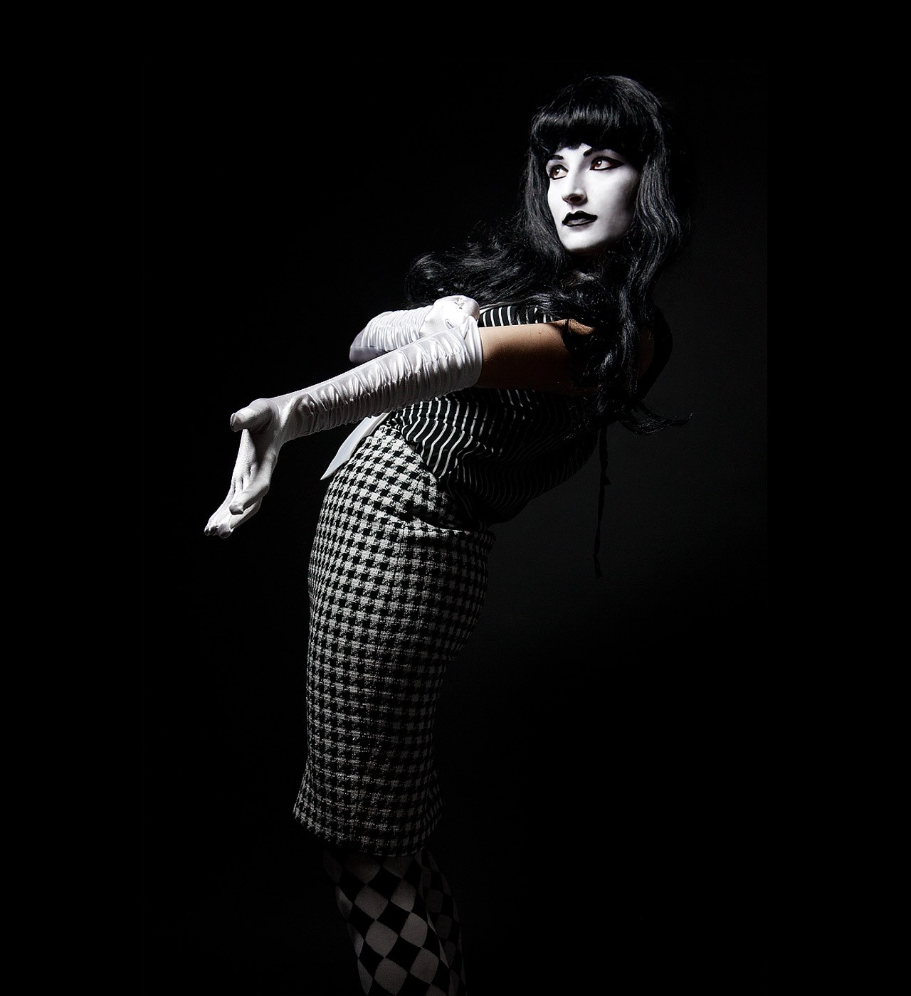 A figure in long white gloves and a houndstooth dress against black