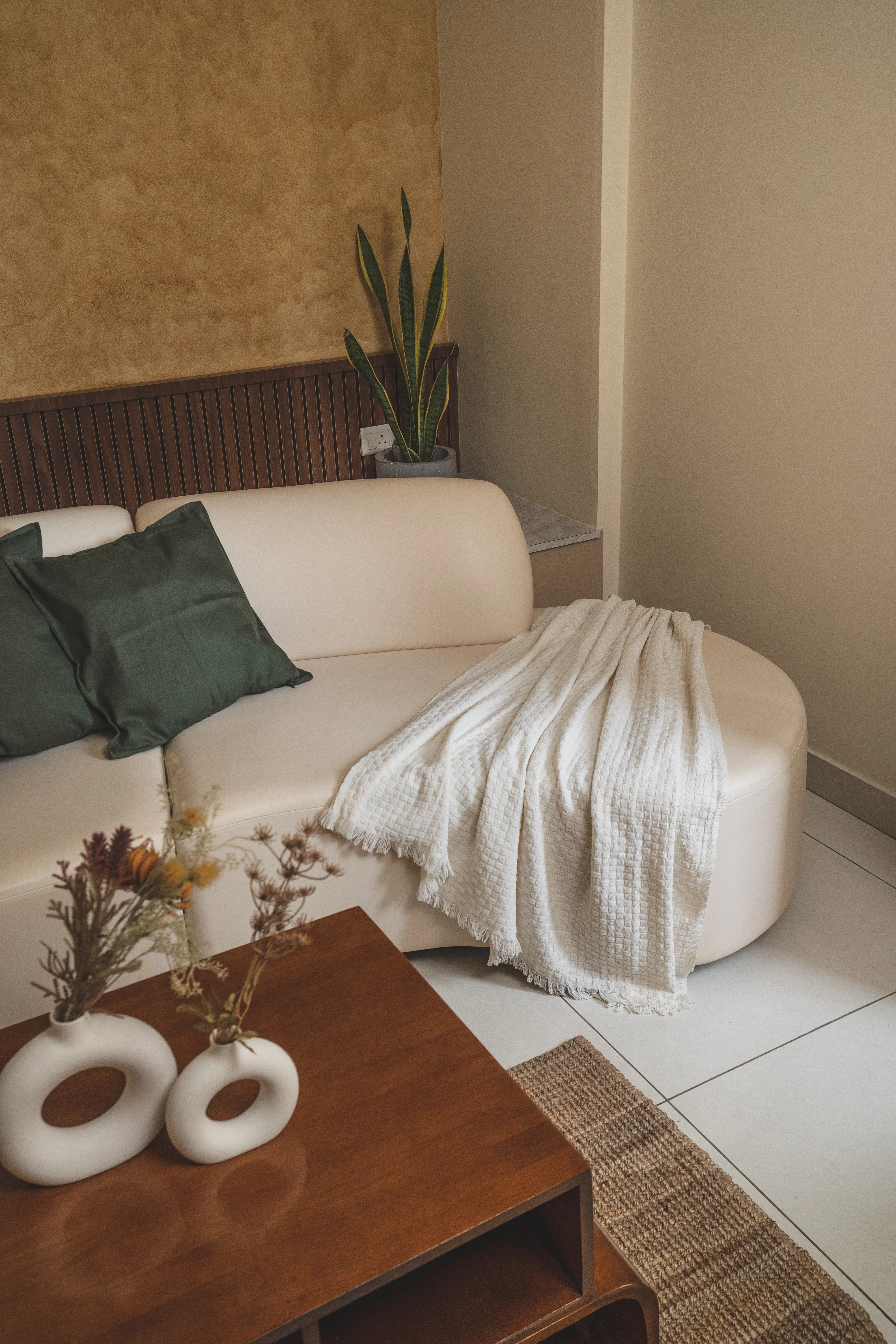 A stylish living room featuring a curved couch, minimalist coffee table, and a decorative wall, designed for South Indian homes.