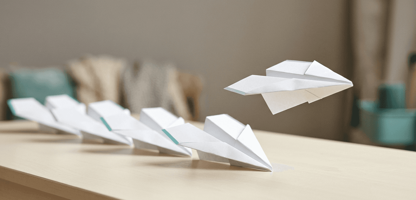 Row of paper airplanes lined up on a desk with one mid-flight
