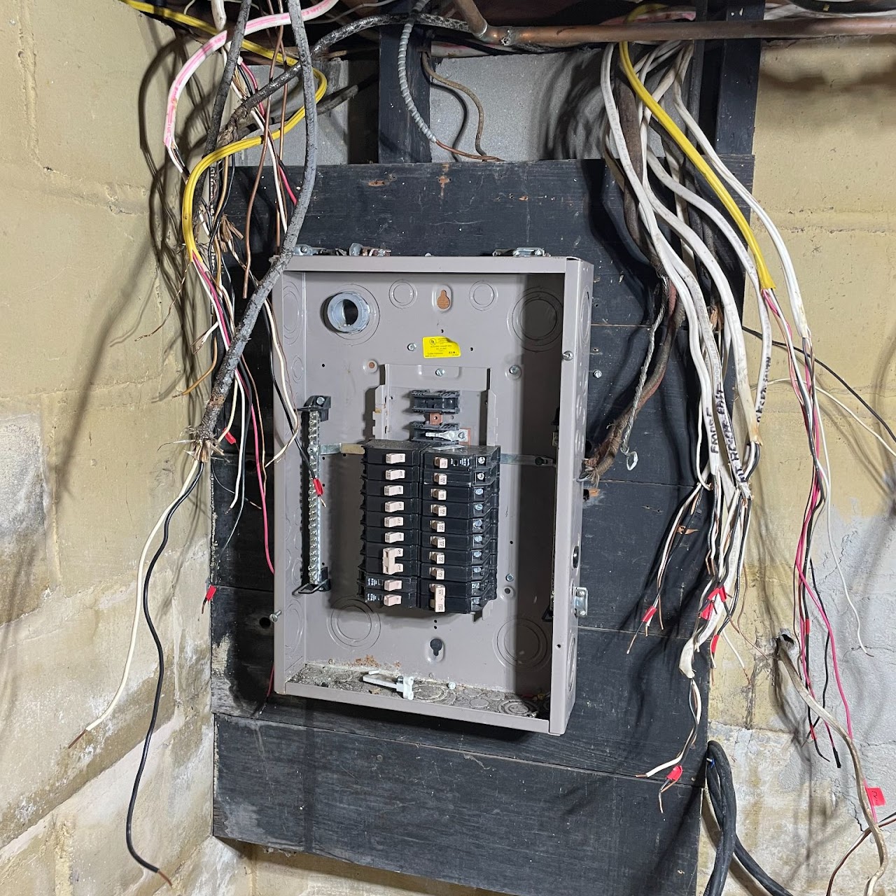 Old open electrical panel with tangled wiring on basement wall