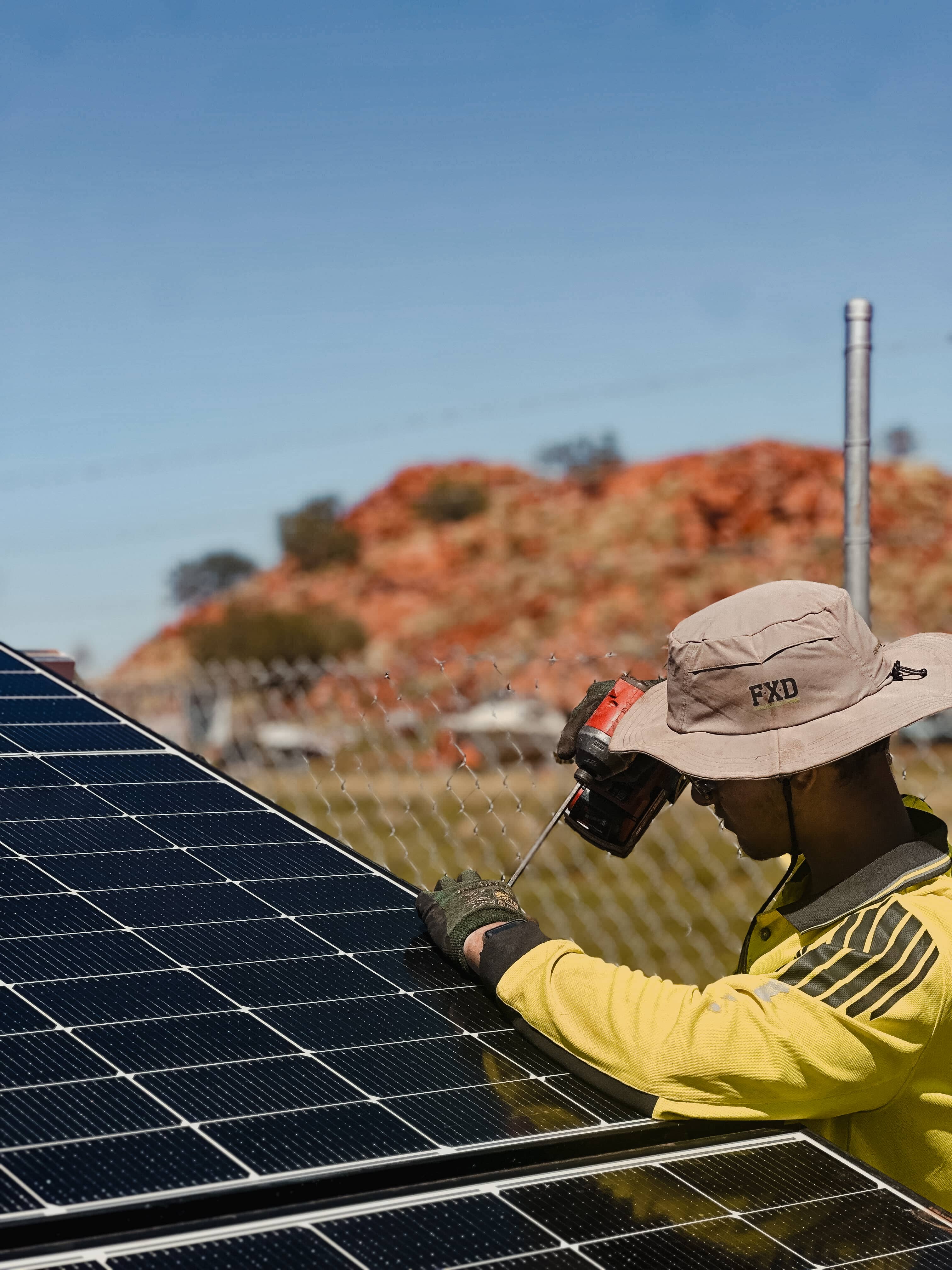 Worker installing solar panels in remote Australia with red hills in background