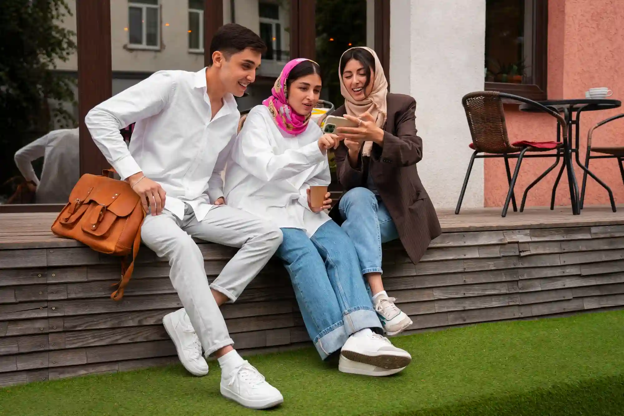A group of friends outdoors sharing a laugh while viewing social media content on a single smartphone screen.