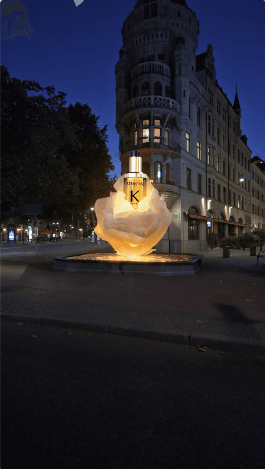 A large, glowing Kérastase hair oil bottle nestled in a translucent flower on a city sidewalk