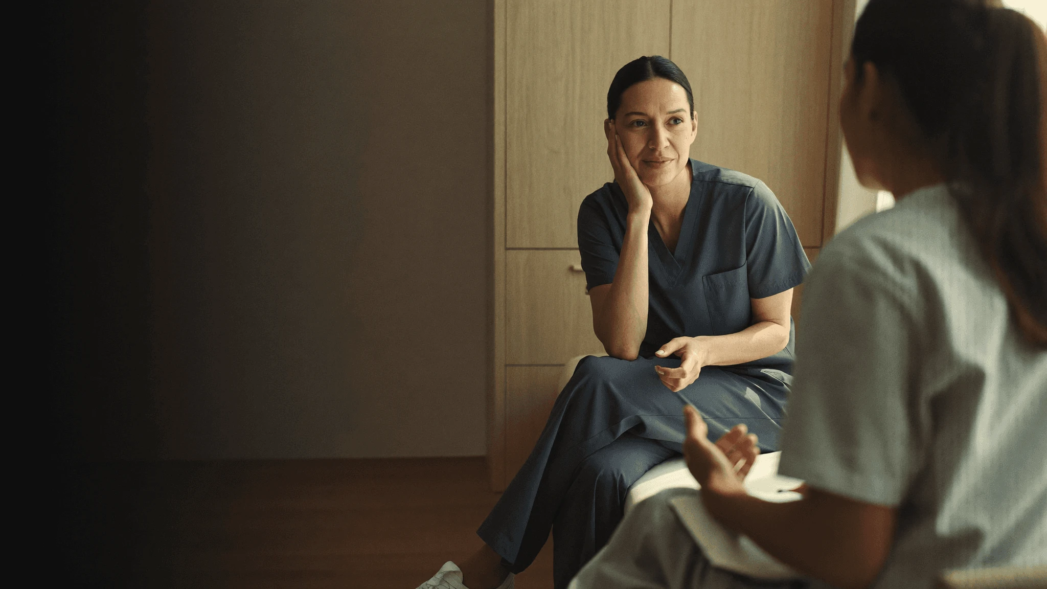 A clinician in scrubs listening to a colleague in a clinic room